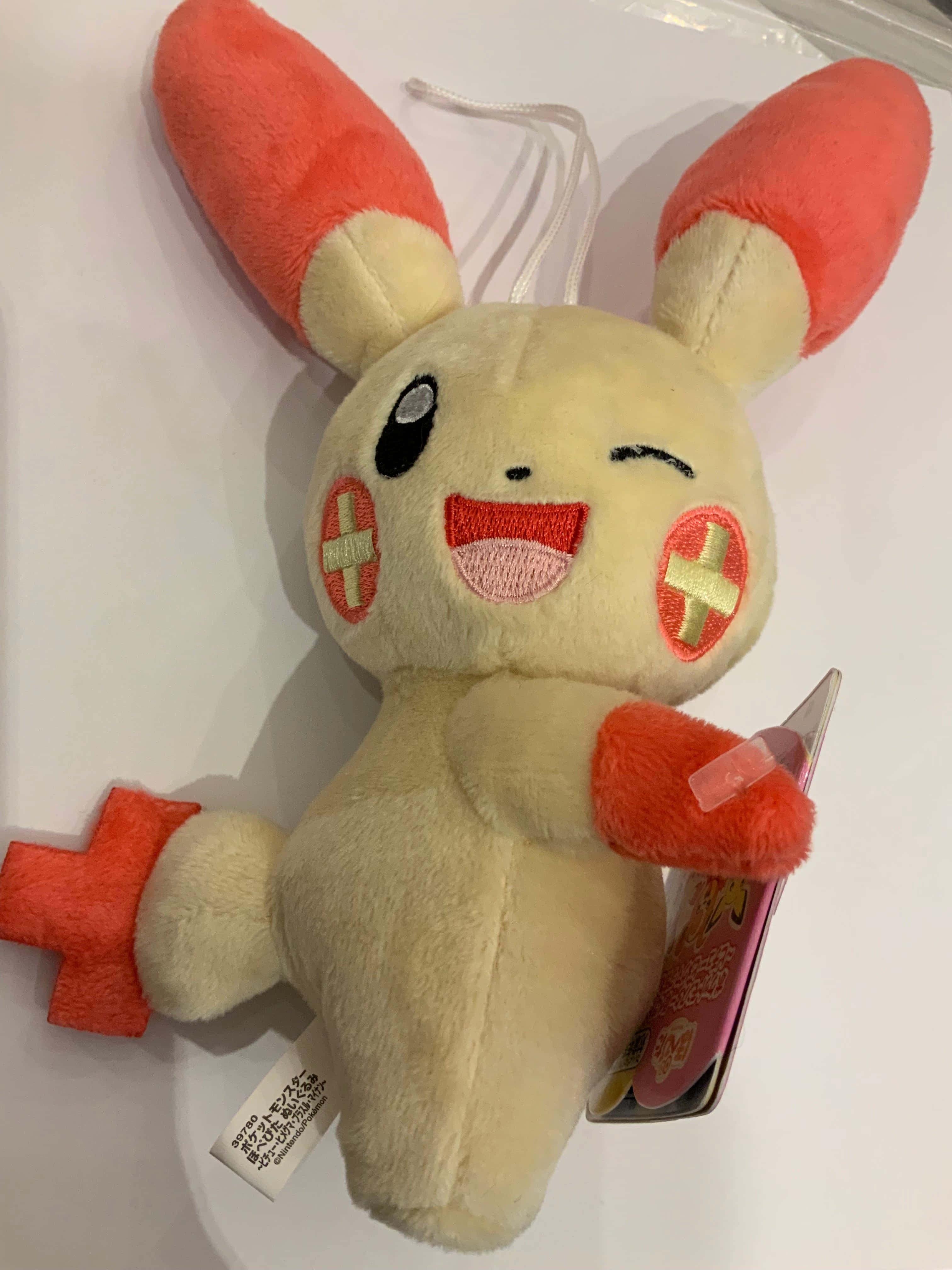 Plusle 桌布 壁紙 — 一個開心的奶油色毛絨玩具，有橙色耳朵和十字補丁，在純白色背景上微笑眨眼。