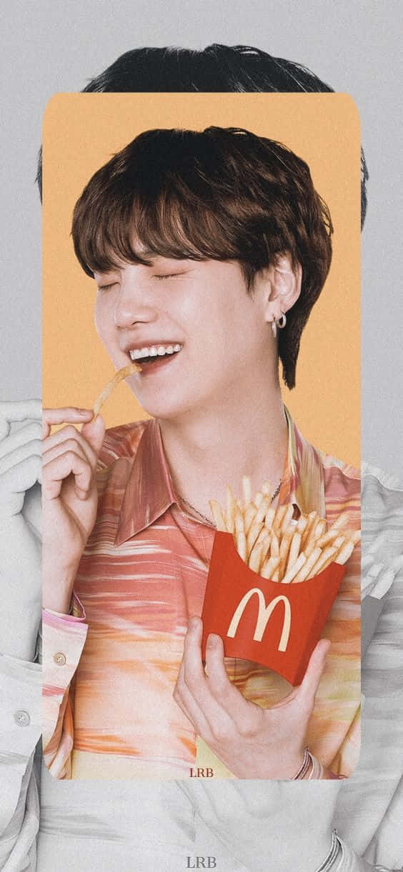 Bts Mac 桌布 壁紙 — 一個開心的年輕男子閉著眼睛微笑，在溫暖的橙色背景前吃著紅色盒子裡的麥當勞薯條。