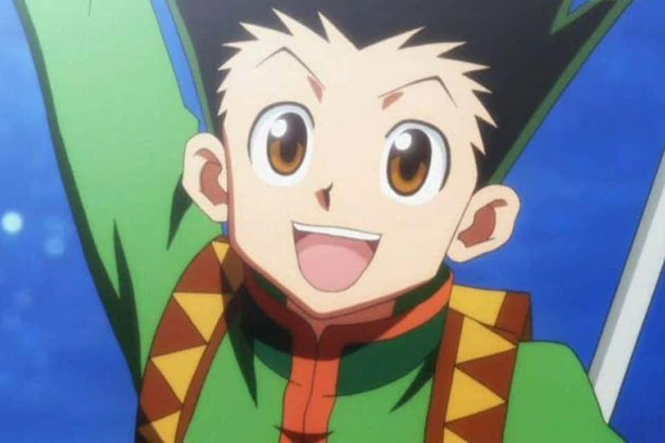 Shonen Anime 桌布 壁紙 — 一個開朗的動畫男孩，有著刺刺的黑髮和寬大的棕色眼睛，穿著綠色和橙色的服裝，燦爛地微笑。