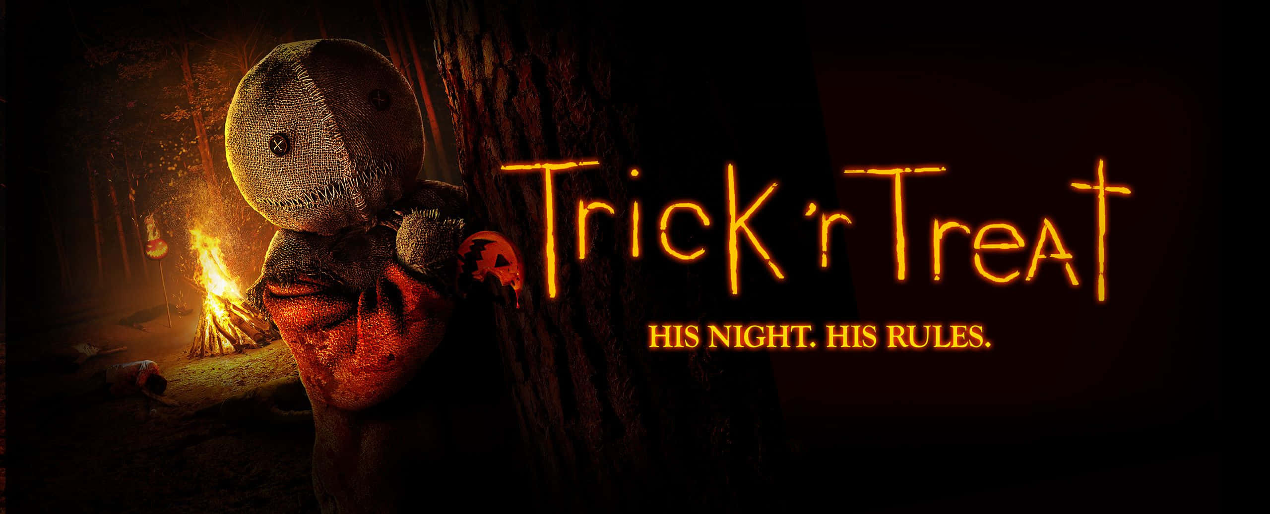 Trick Or Treat 桌布 壁紙 — 一個陰森的縫製娃娃從黑暗森林中的一棵樹後探出頭來，營火照亮了森林，並有發光的橙色文字寫著 Trick r Treat。