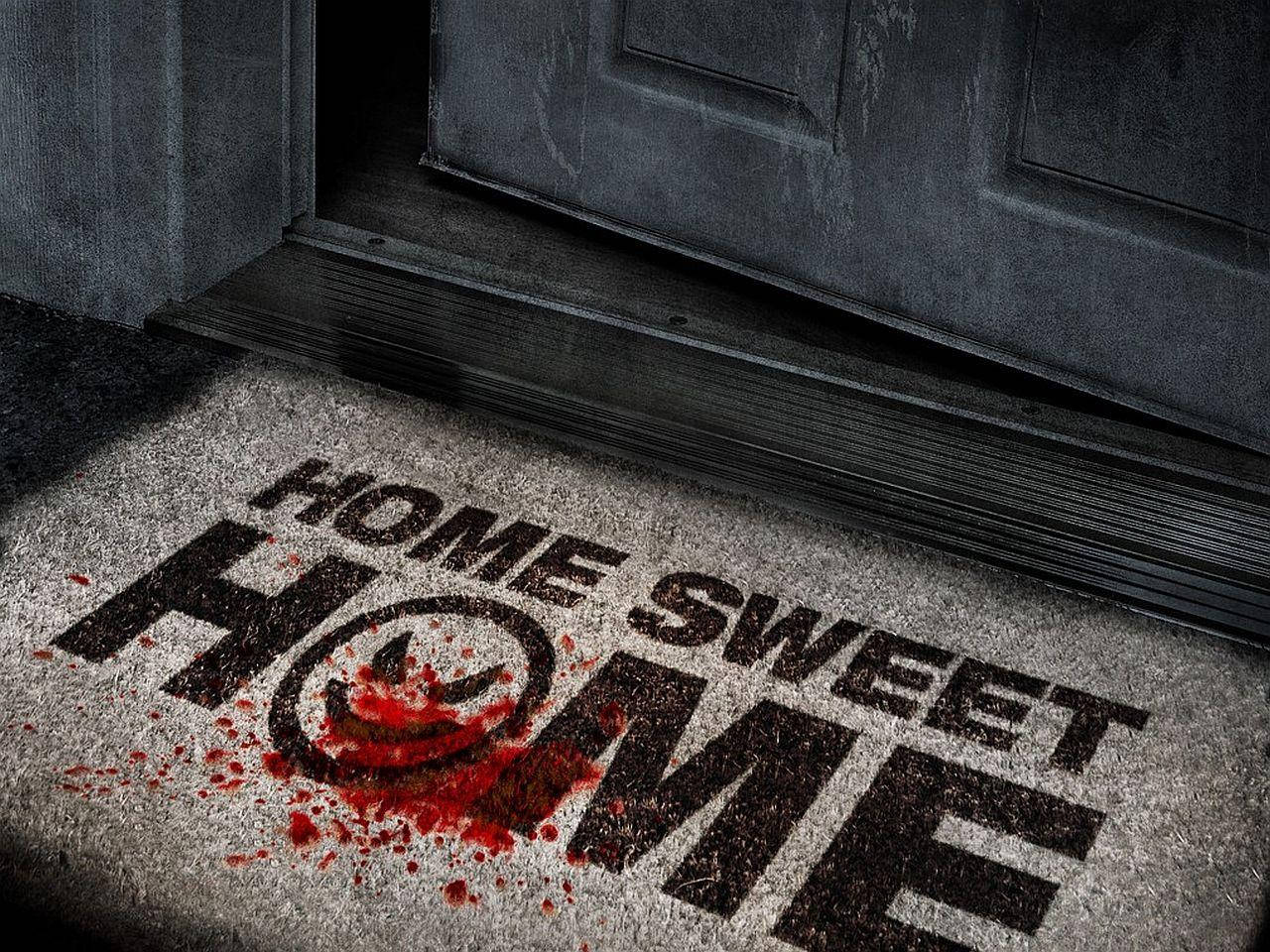 甜蜜的家 桌布 壁紙 — 一個陰森的門墊，上面有「HOME SWEET HOME」字樣，在黑暗門口附近濺滿血跡。