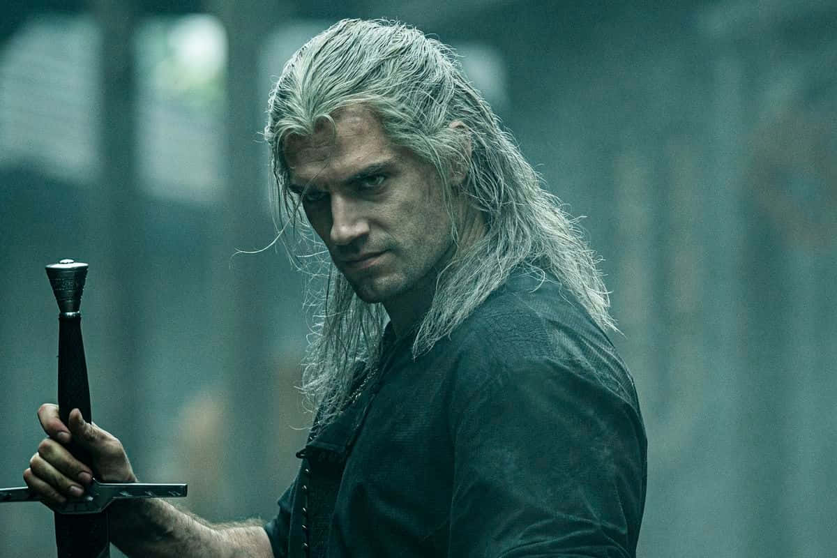 The Witcher Characters 桌布 壁紙 — 一個陰沉的戰士，長長銀髮，在迷霧籠罩、青綠色的森林空地中緊握一把劍。
