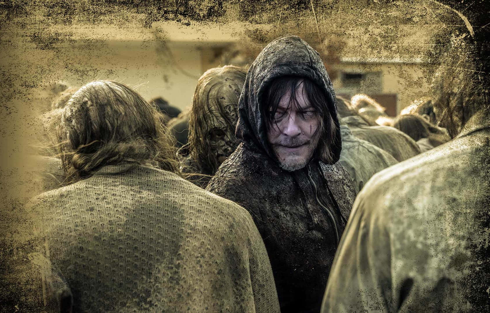 walking dead 桌布 壁紙 — 一個陰沉的男人穿著連帽外套，站在一群骯髒的人群中，處於荒涼而粗糙的環境。