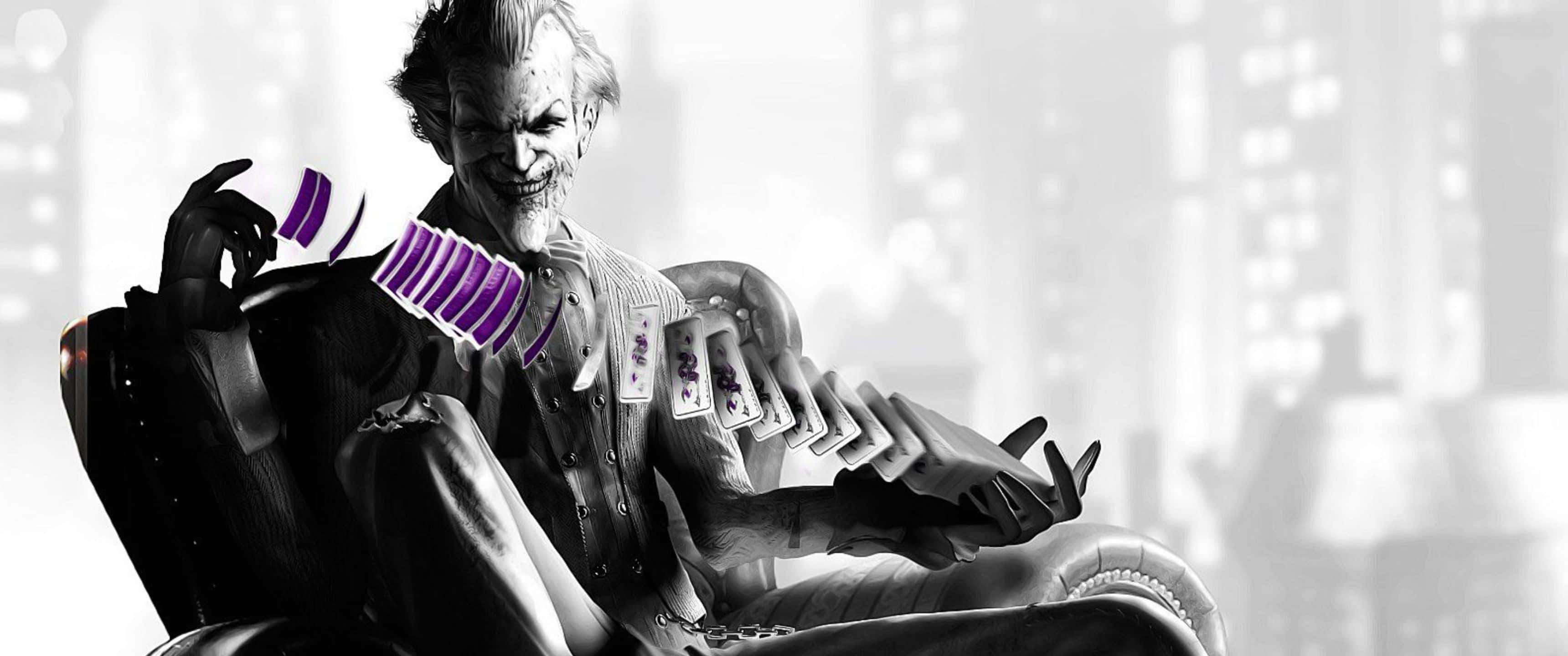 3440x1440p Batman Arkham City 桌布 壁紙 — 一個陰險的小丑坐在椅子上，手持紫色撲克牌，背景是模糊的城市天際線。