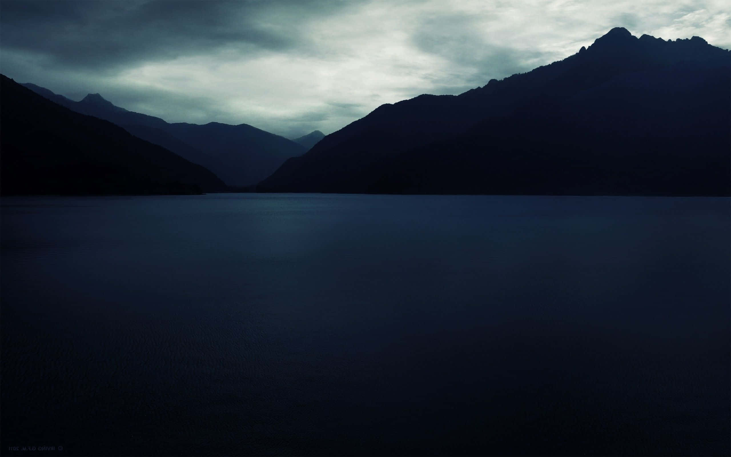 Dark Landscape 桌布 壁紙 — 一個陰鬱的暮色湖泊，坐落於陰暗山巒剪影之間，天空多雲。
