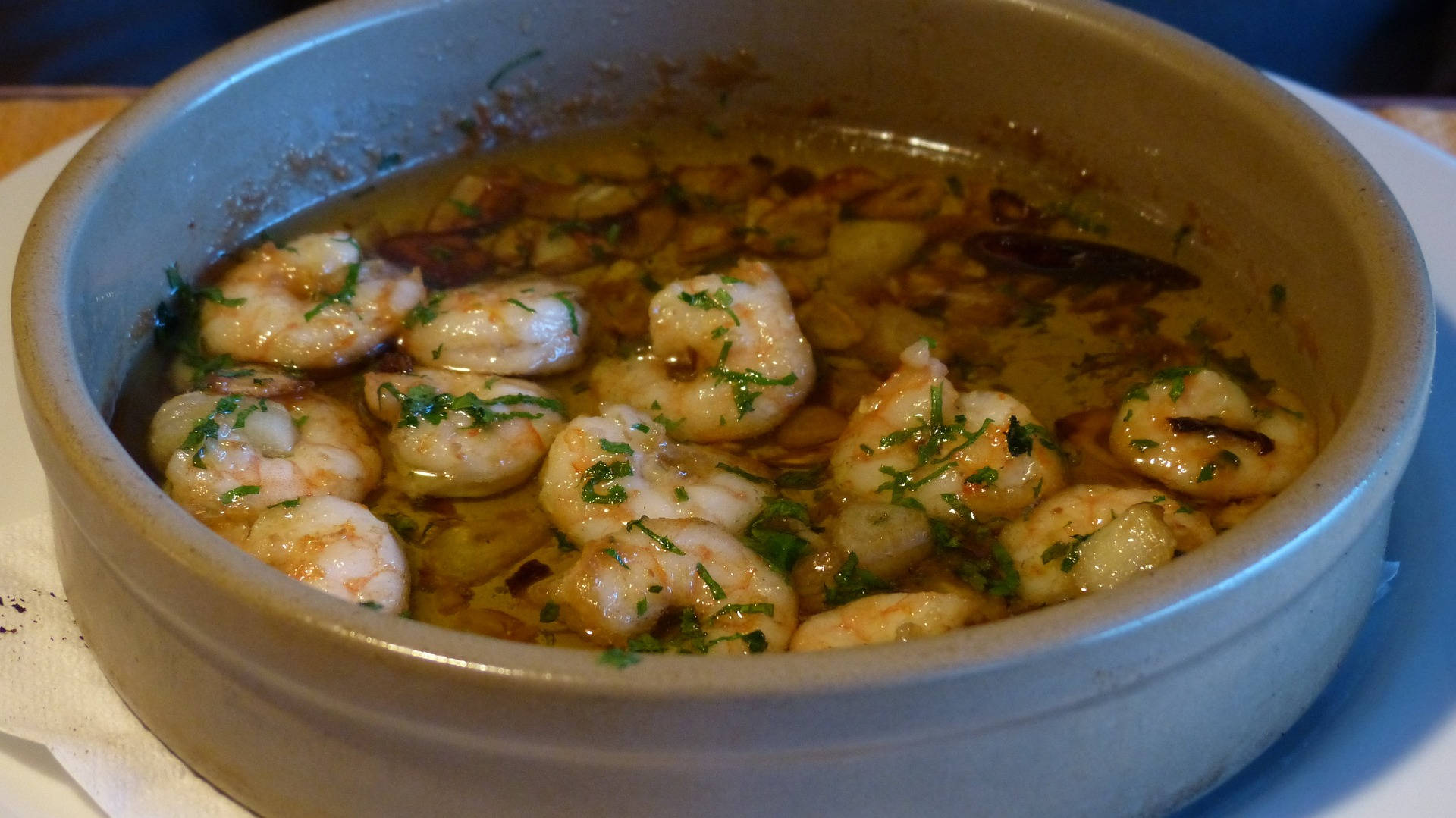 Seafood 桌布 壁紙 — 一個陶瓷碗盛載著多汁的蝦，浸泡在蒜油中，並以新鮮歐芹點綴。