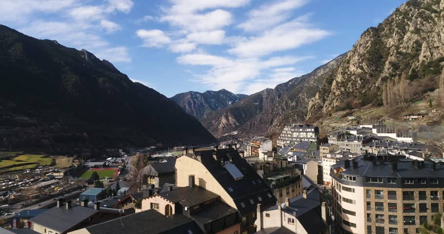 城市 桌布 壁紙 — 一個陽光明媚的山村，坐落在一個山谷中，有陡峭的岩石懸崖和散落的建築物，在藍天白雲下。