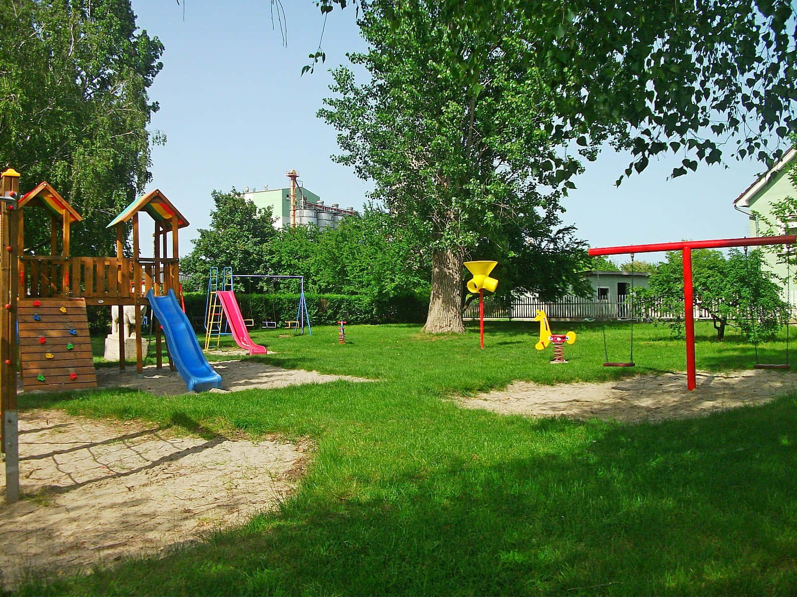 Playground 桌布 壁紙 — 一個陽光明媚的戶外遊樂場，設有色彩繽紛的溜滑梯、鞦韆和攀爬設施，周圍環繞著綠草和枝葉茂密的樹木。