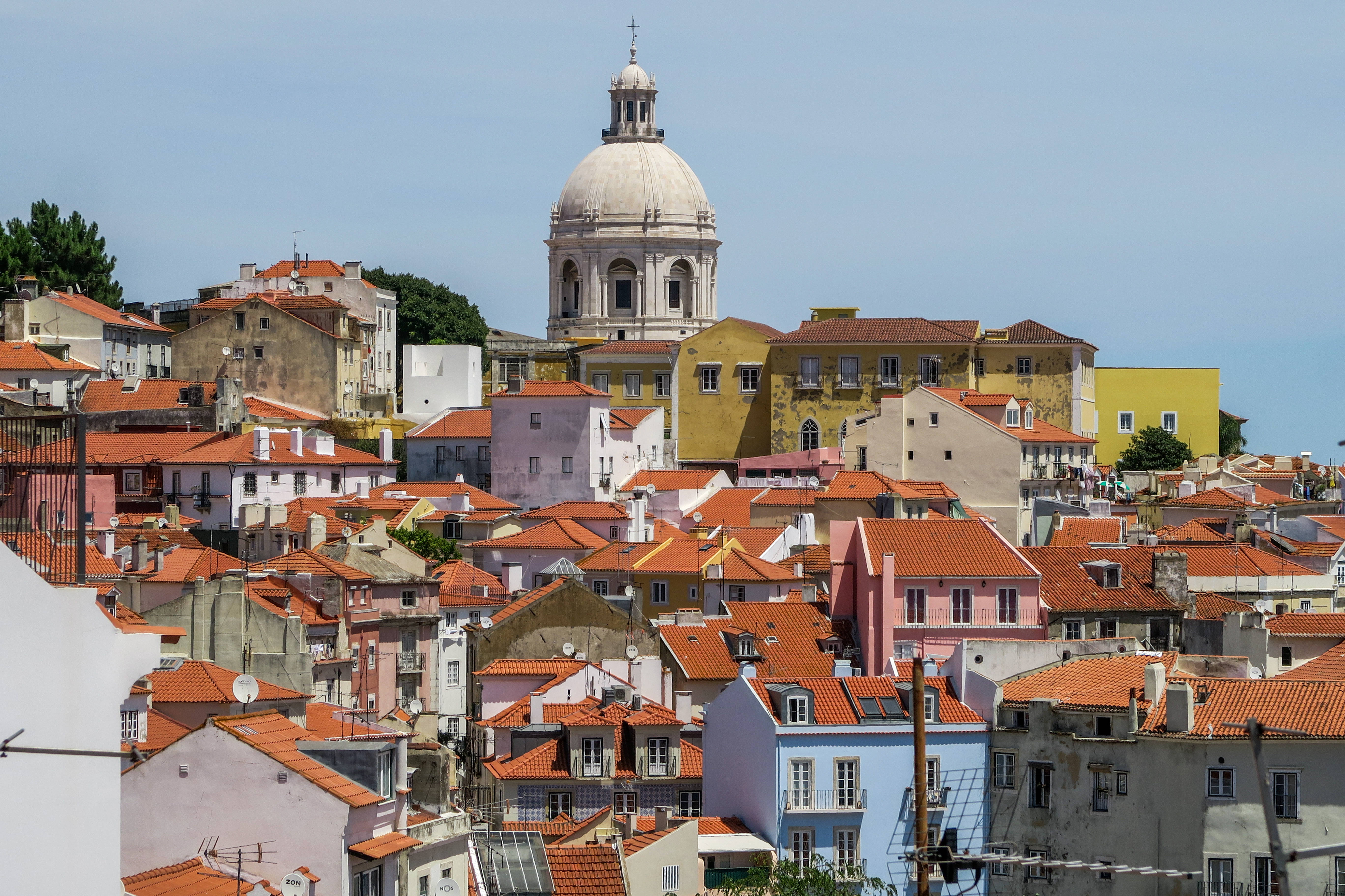 Portugal 桌布 壁紙 — 一個陽光普照的山丘小鎮，擁有陶土屋頂和粉彩建築，在清澈的藍天下有一座白色圓頂教堂。