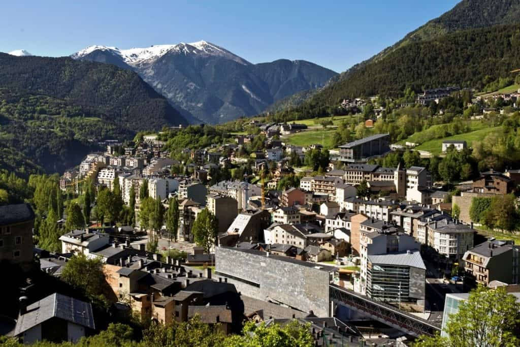 山脈 桌布 壁紙 — 一個陽光普照的山村，坐落在山谷中，背後有白雪覆蓋的山峰聳立。