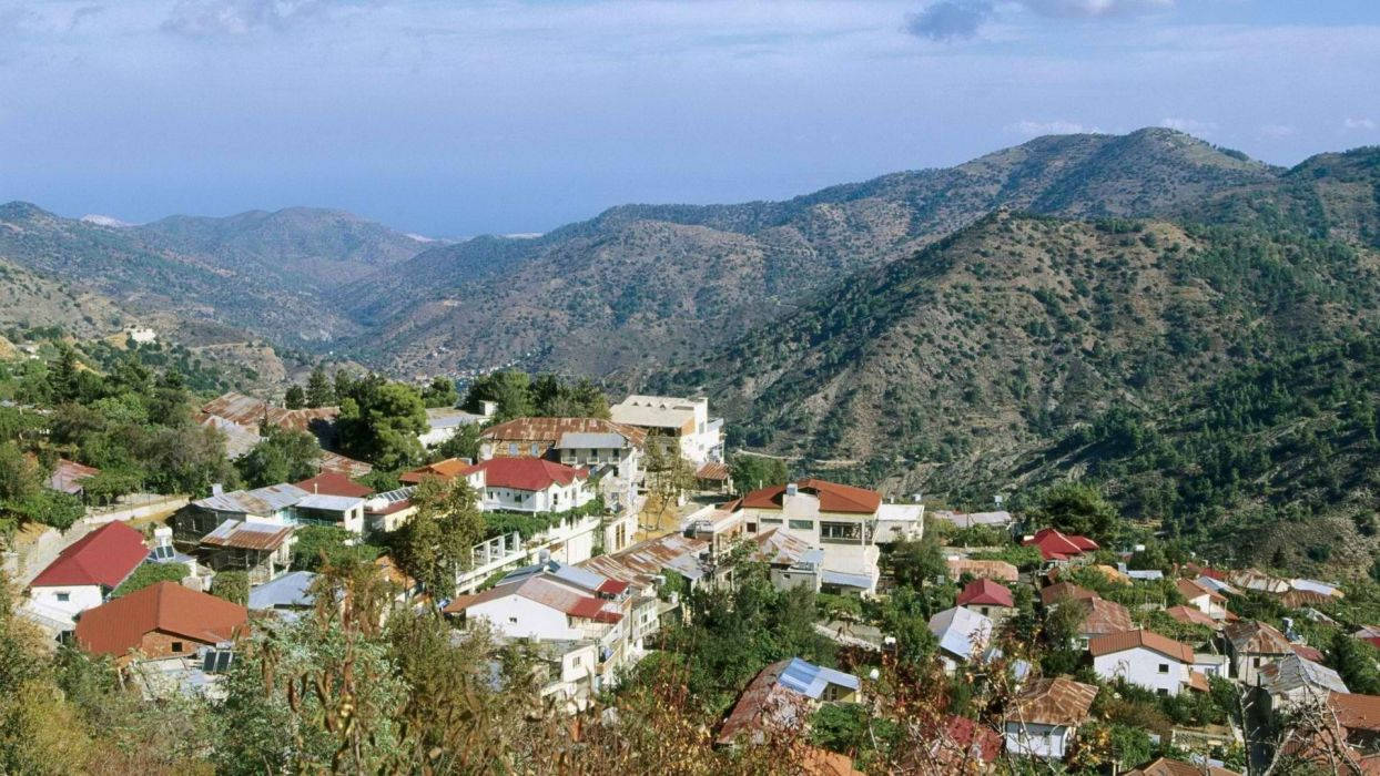 Cyprus 桌布 壁紙 — 一個陽光普照的山邊村莊，擁有陶土屋頂，坐落在俯瞰大海的綠色山脈之中。