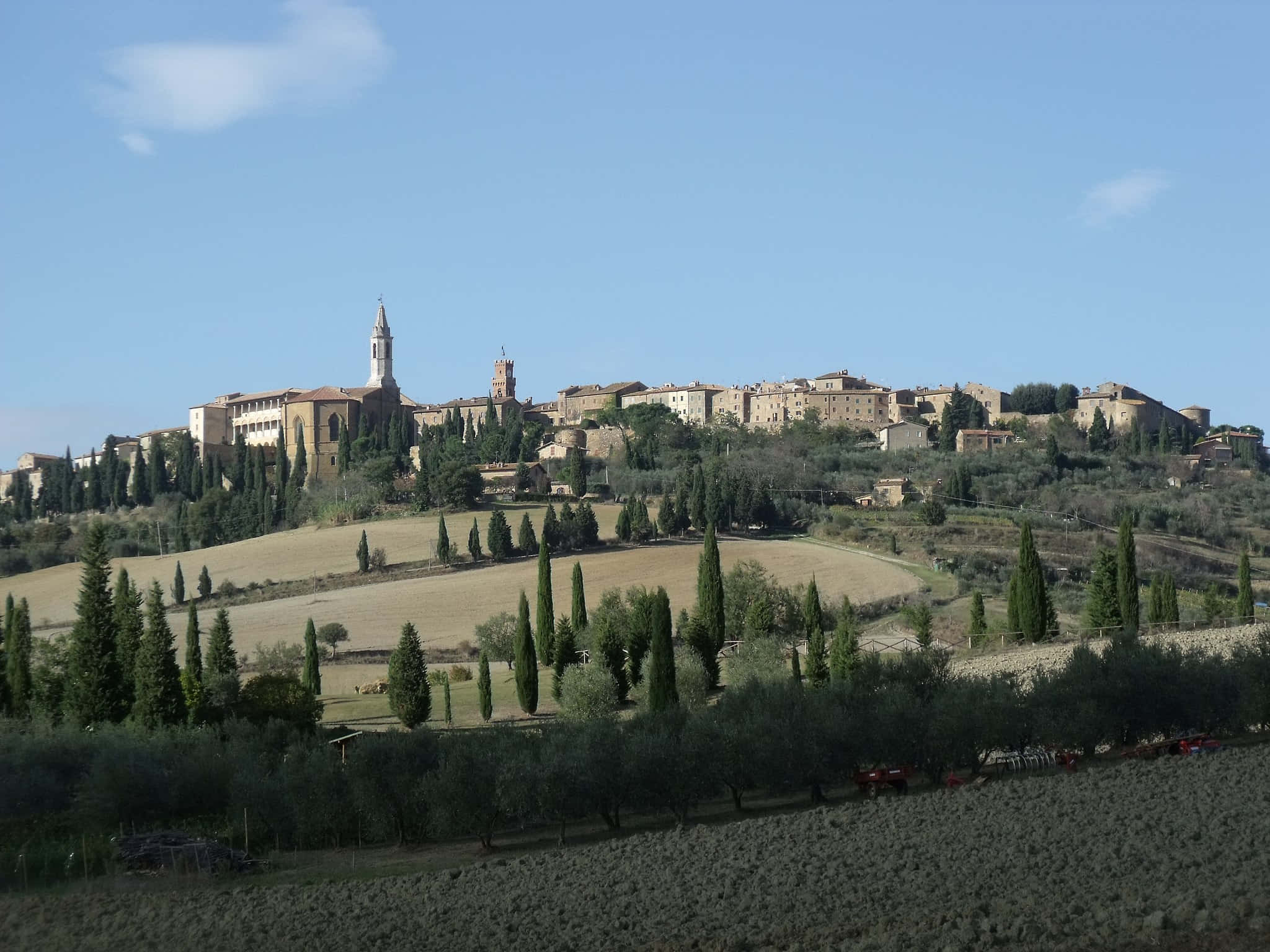 Tuscany 桌布 壁紙 — 一個陽光普照的山頂村莊，擁有石頭建築和教堂塔樓，俯瞰著梯田和高大的柏樹，天空清澈湛藍。