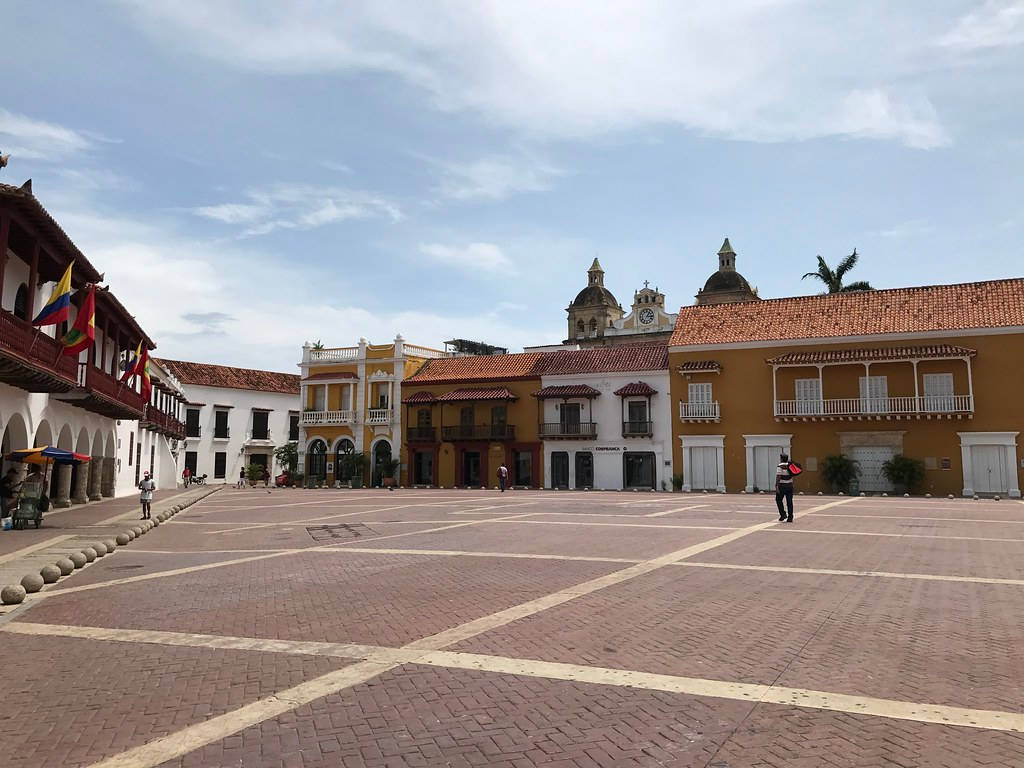 Colombia 桌布 壁紙 — 一個陽光普照的殖民風格廣場，擁有赤陶屋頂建築和鐘樓，天空部分多雲。