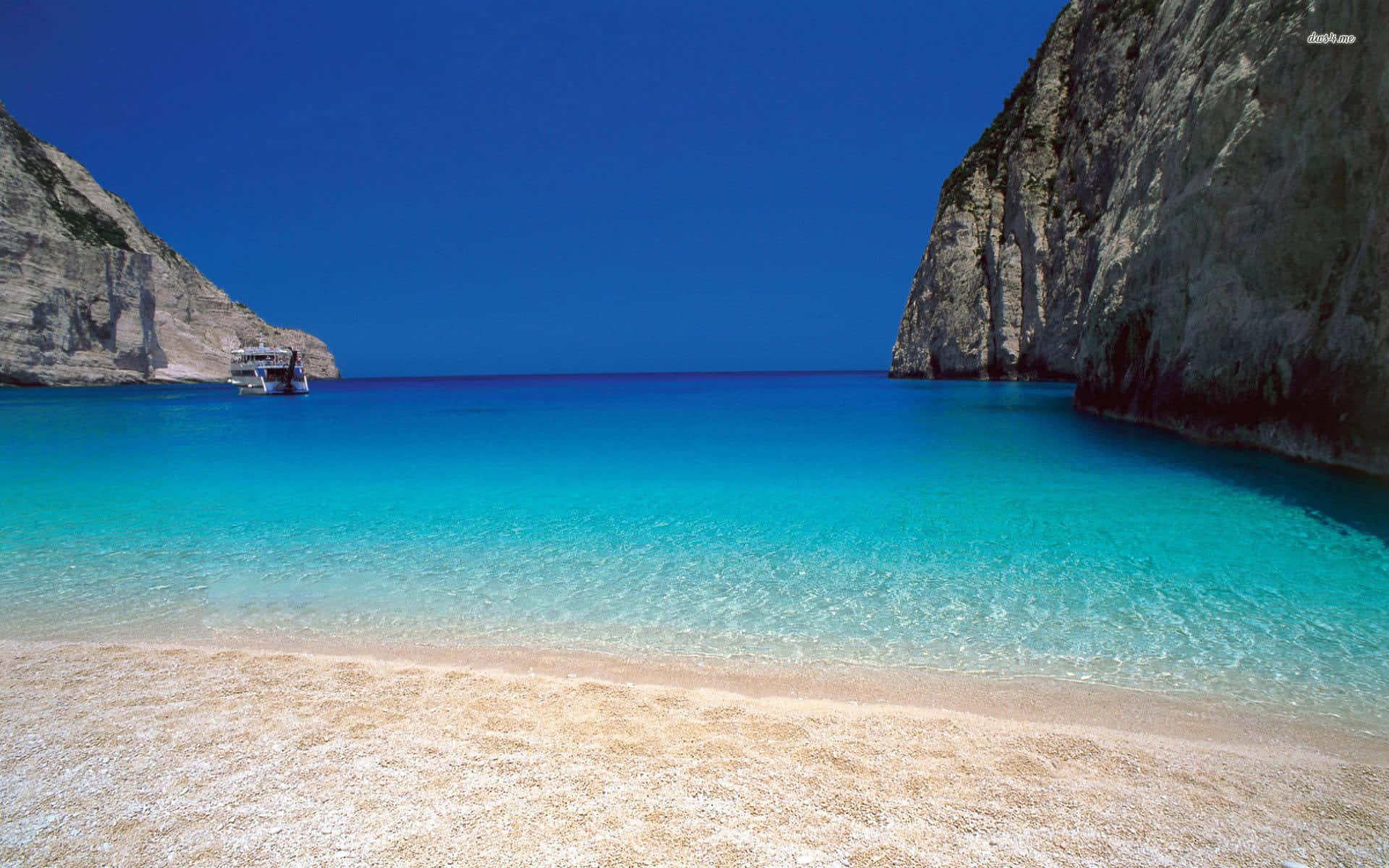 Greek Beach 桌布 壁紙 — 一個隱世海灘，碧綠清澈的海水被高聳的懸崖環繞，上方是湛藍的天空。