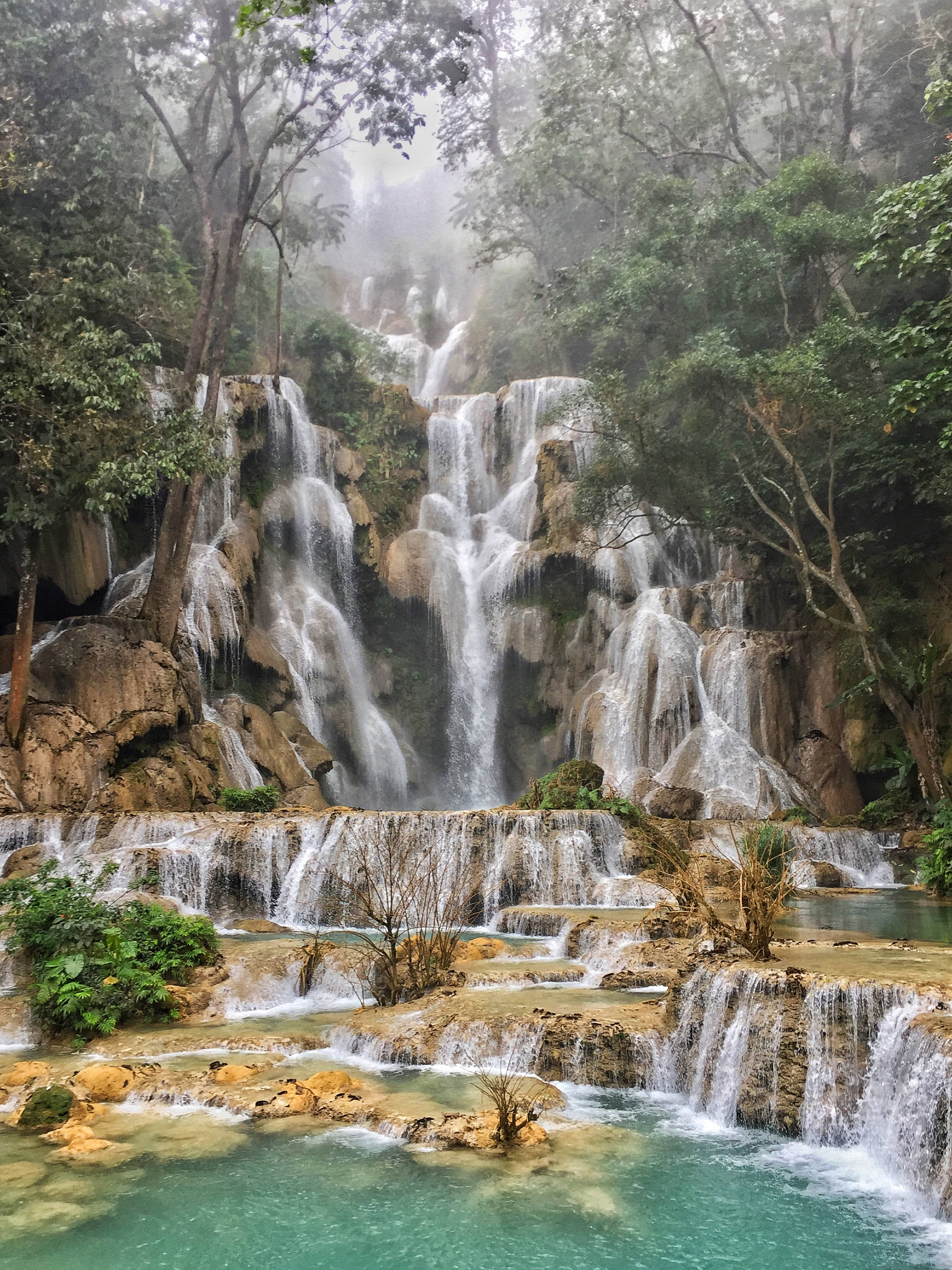 Laos 桌布 壁紙 — 一個雄偉的多層瀑布穿過茂密的綠色叢林，傾瀉而下，流入下方的碧綠水池。