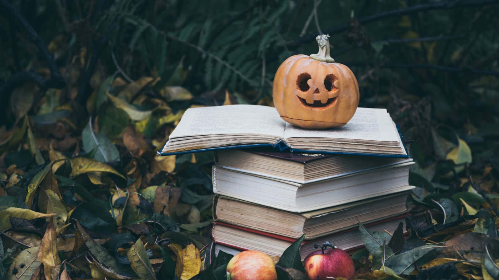 Halloween Books 桌布 壁紙 — 一個雕刻的南瓜燈放在一堆被落葉和蘋果包圍的書本上。