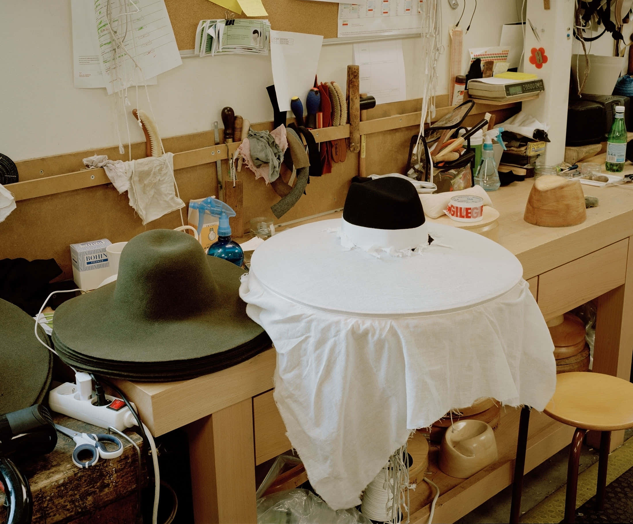Clothes 桌布 壁紙 — 一個雜亂的帽子工坊，木製工作台上放著處於不同製作階段的氈帽。