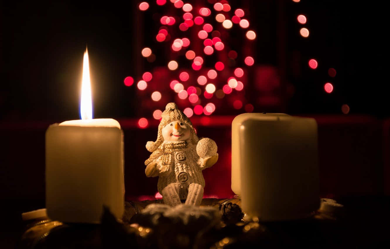 Advent 桌布 壁紙 — 一個雪人公仔坐在兩根點燃的蠟燭之間，背景黑暗中有紅色燈光的散景。