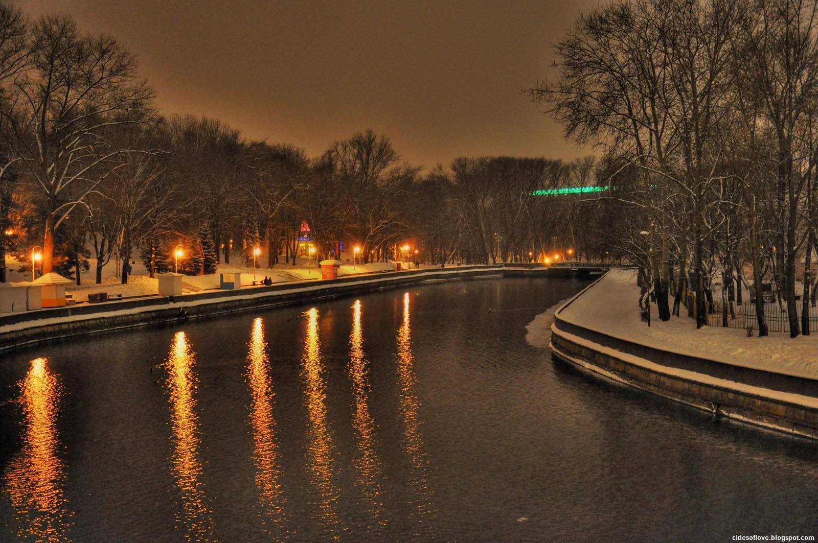 Winter 桌布 壁紙 — 一個雪白的冬夜，沿著平靜的運河，溫暖的路燈倒映在水面上，光禿禿的樹木排列在兩岸。
