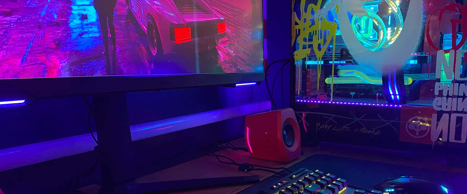 Gaming Pc Setup 桌布 壁紙 — 一個霓虹燈光下的電競設置，發光的顯示器顯示一輛汽車在雨濕的街道上行駛，以及一部帶有鮮豔RGB燈光的自訂電腦。