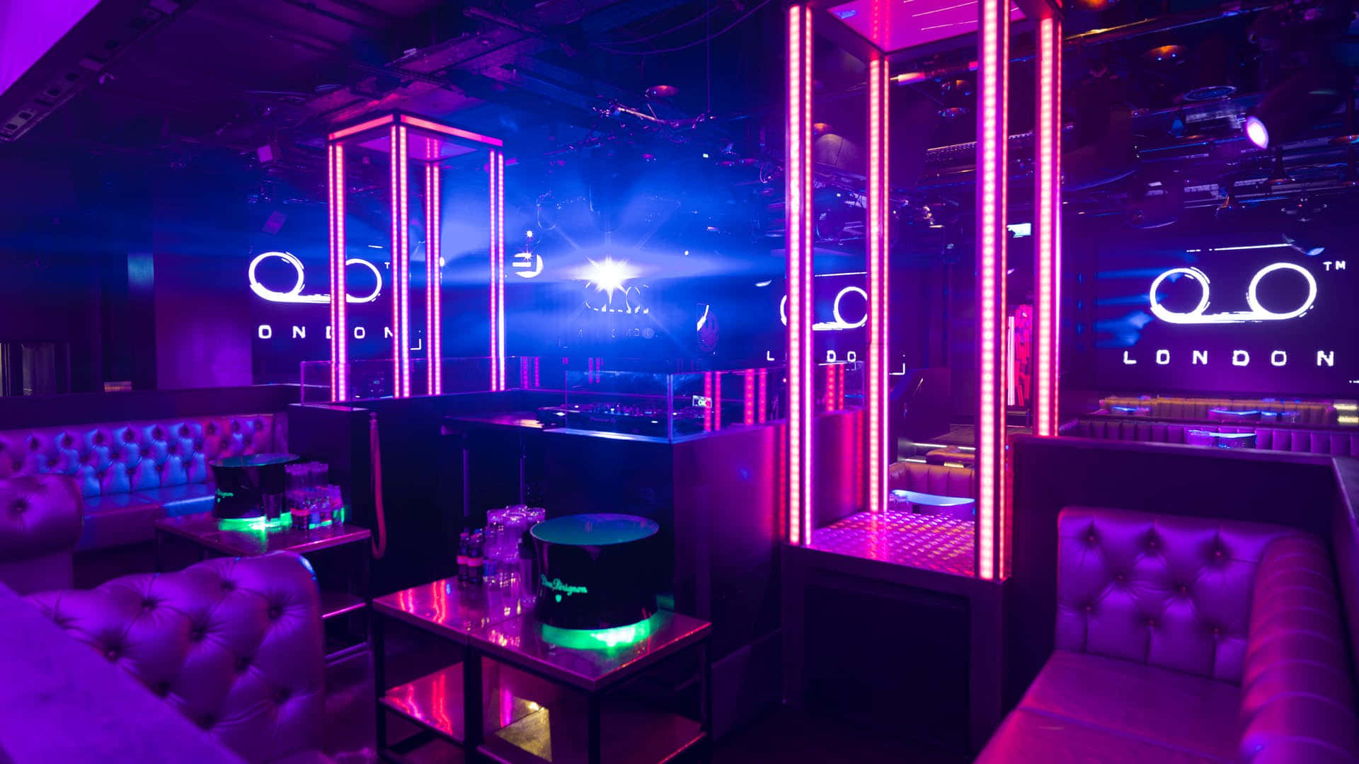 club 桌布 壁紙 — 一個霓虹燈夜總會休息室，配有簇絨卡座，在紫色和粉紅色燈光下閃耀。