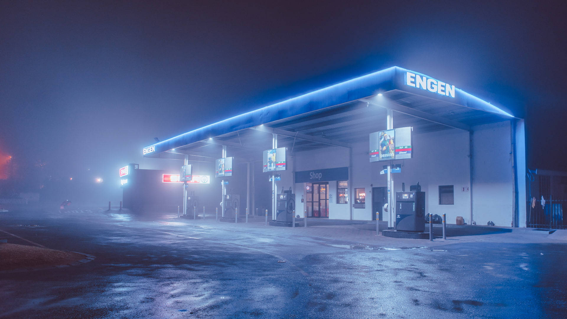 Gas Station 桌布 壁紙 — 一個霧夜，英根加油站發出藍色霓虹燈光，映照在濕漉漉的路面上。
