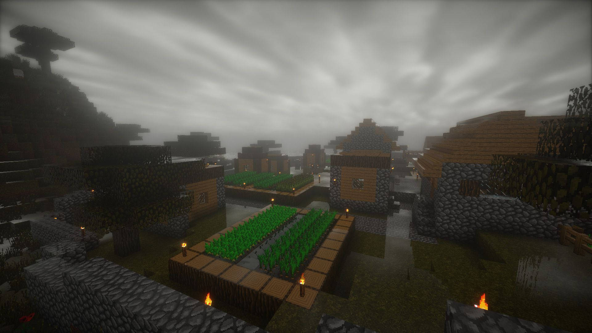 Minecraft Aesthetic 桌布 壁紙 — 一個霧氣瀰漫的Minecraft村莊，有木屋、石牆和火把在陰天天空下發光。