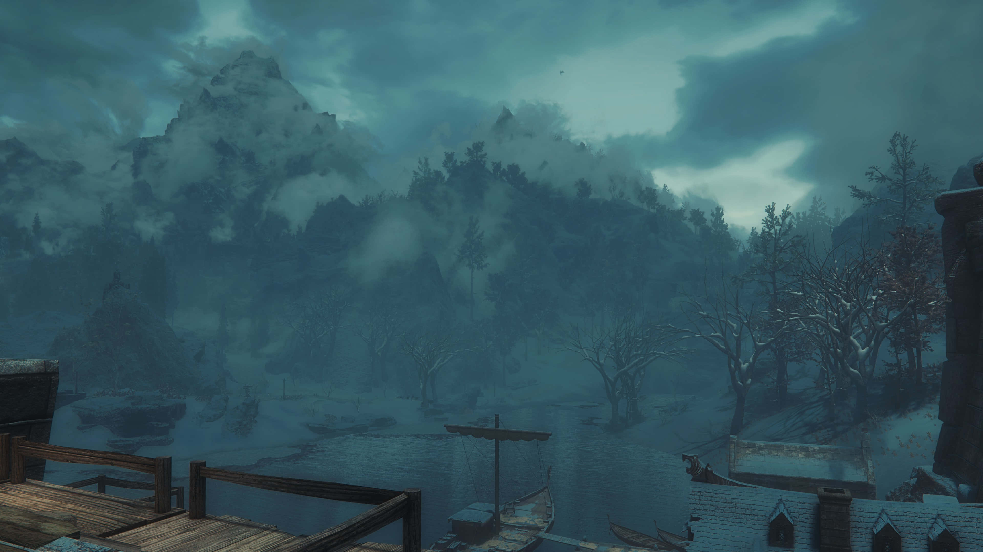 Skyrim Windhelm 桌布 壁紙 — 一個霧氣瀰漫的冬季村莊，坐落在一條結冰的河邊，屋頂覆蓋著白雪，光禿禿的樹木在陰鬱的藍綠色天空下。