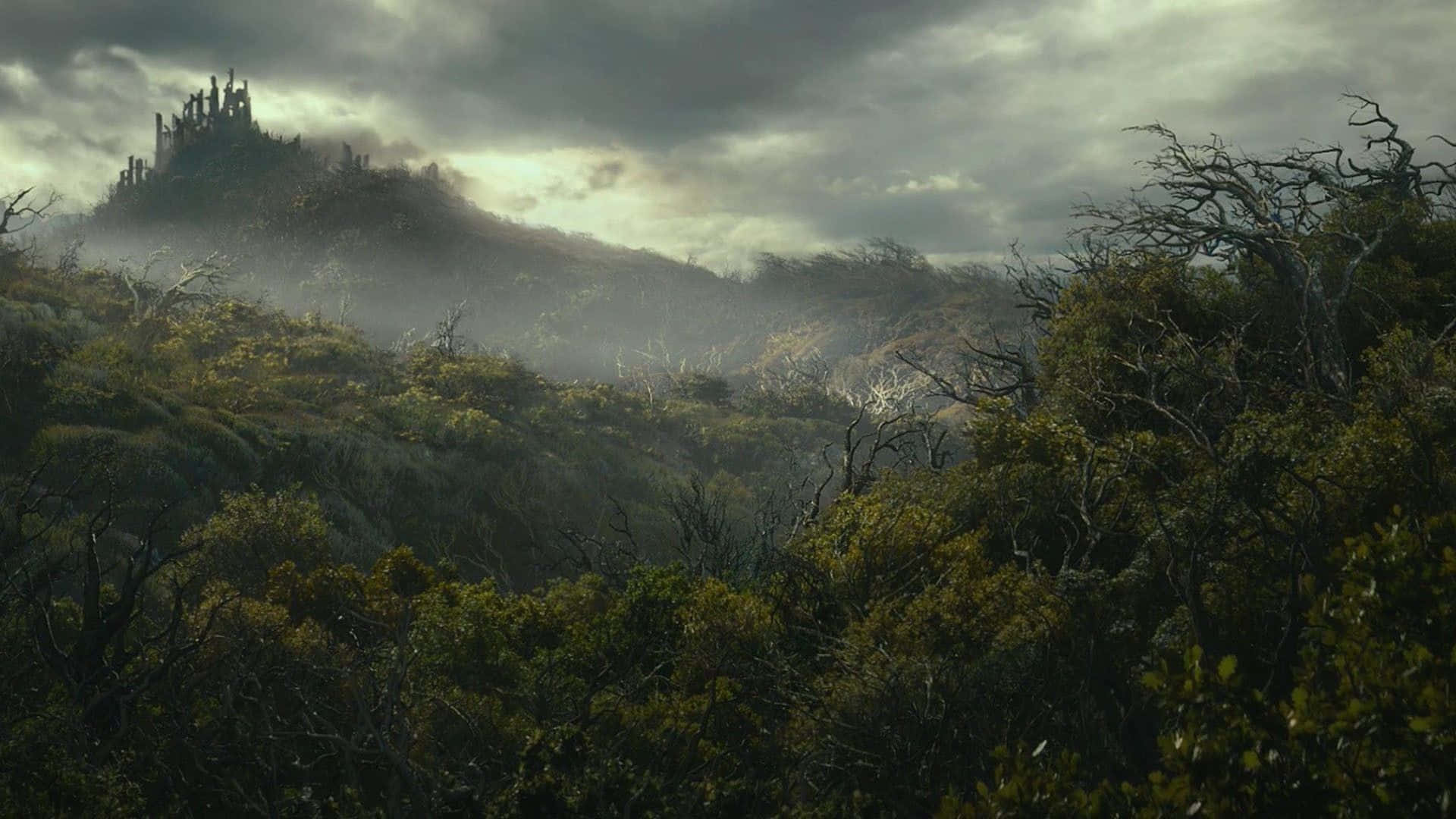 Lotr 桌布 壁紙 — 一個霧氣瀰漫的山景，山頂上有一座搖搖欲墜的城堡，天空風暴來襲。
