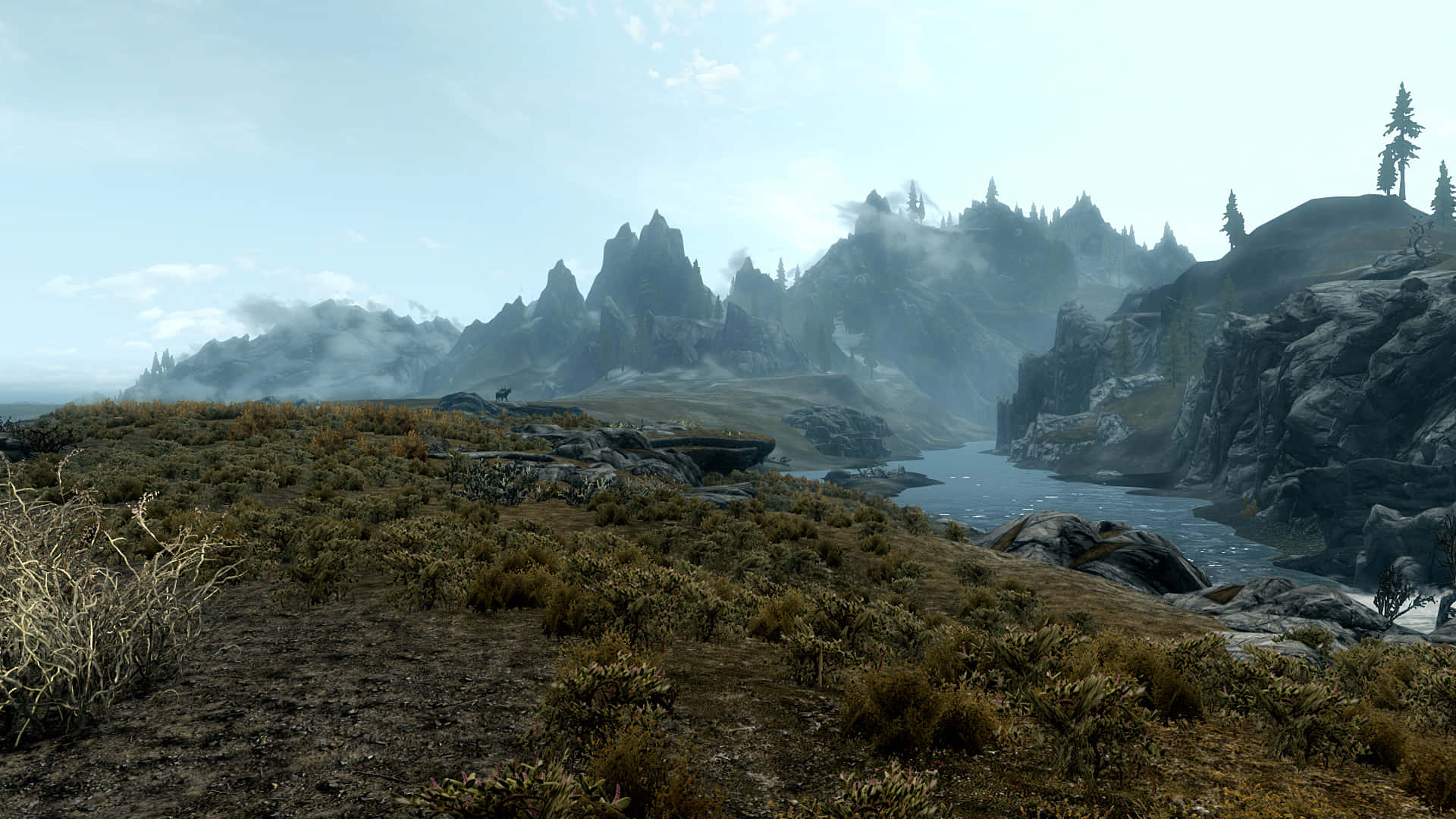 Skyrim Landscapes 桌布 壁紙 — 一個霧氣瀰漫的山谷，蜿蜒的河流兩旁是崎嶇的懸崖和稀疏的植被，天空蒼白。