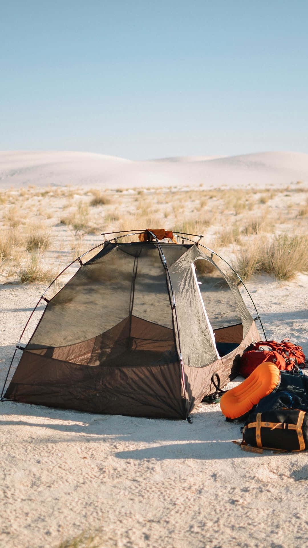 Minimalist Camping 桌布 壁紙 — 一個露營帳篷和裝備在廣闊的沙漠中，伴隨著起伏的沙丘，在清澈的藍天下休息。