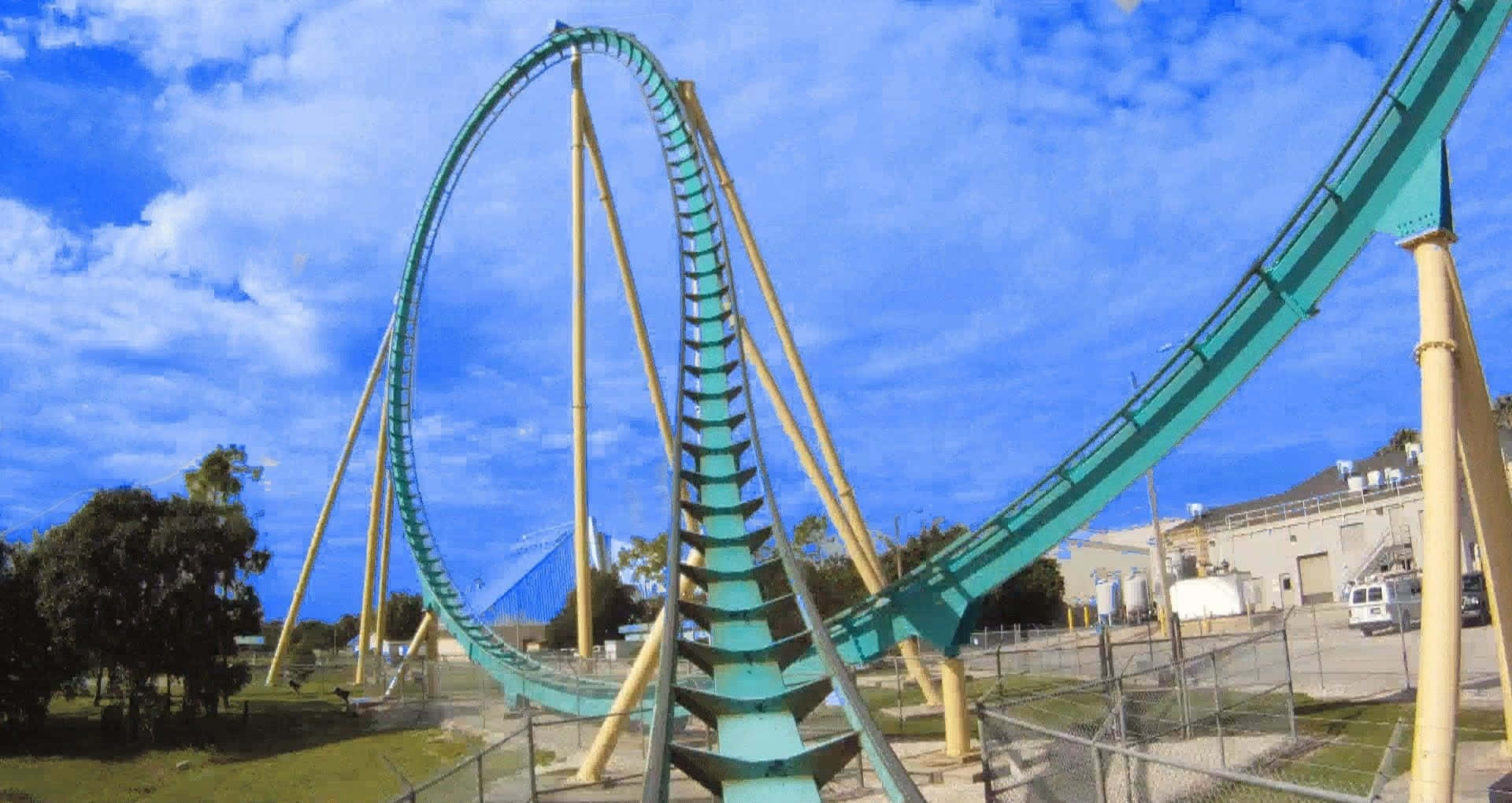 Roller Coaster 桌布 壁紙 — 一個青綠色的雲霄飛車，黃色支架在有零星白雲的明亮藍天下戲劇性地拱起。