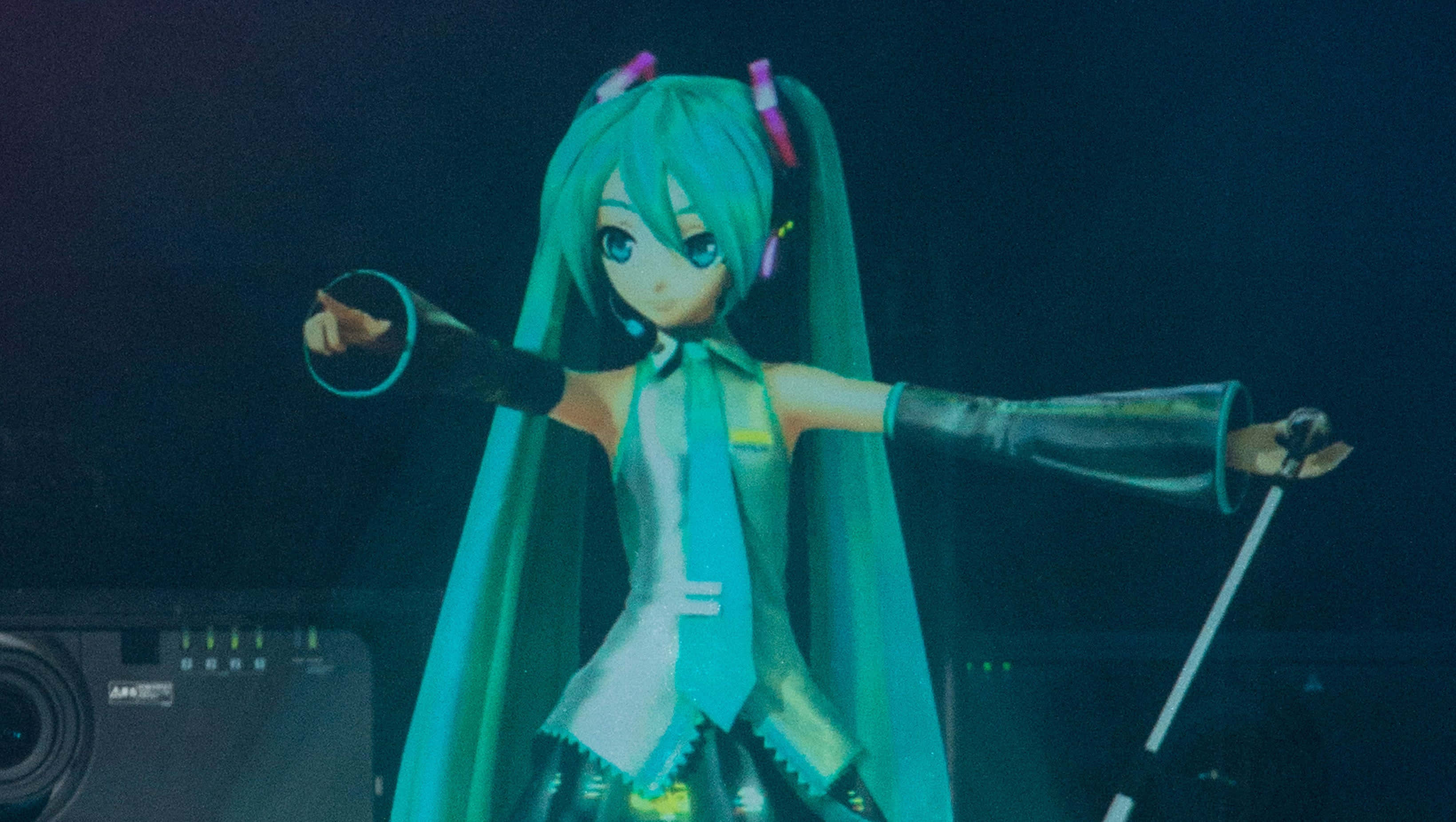 初音未來 桌布 壁紙 — 一個青綠色頭髮的動漫角色在藍色燈光下在舞台上表演，雙臂伸展，手持麥克風。