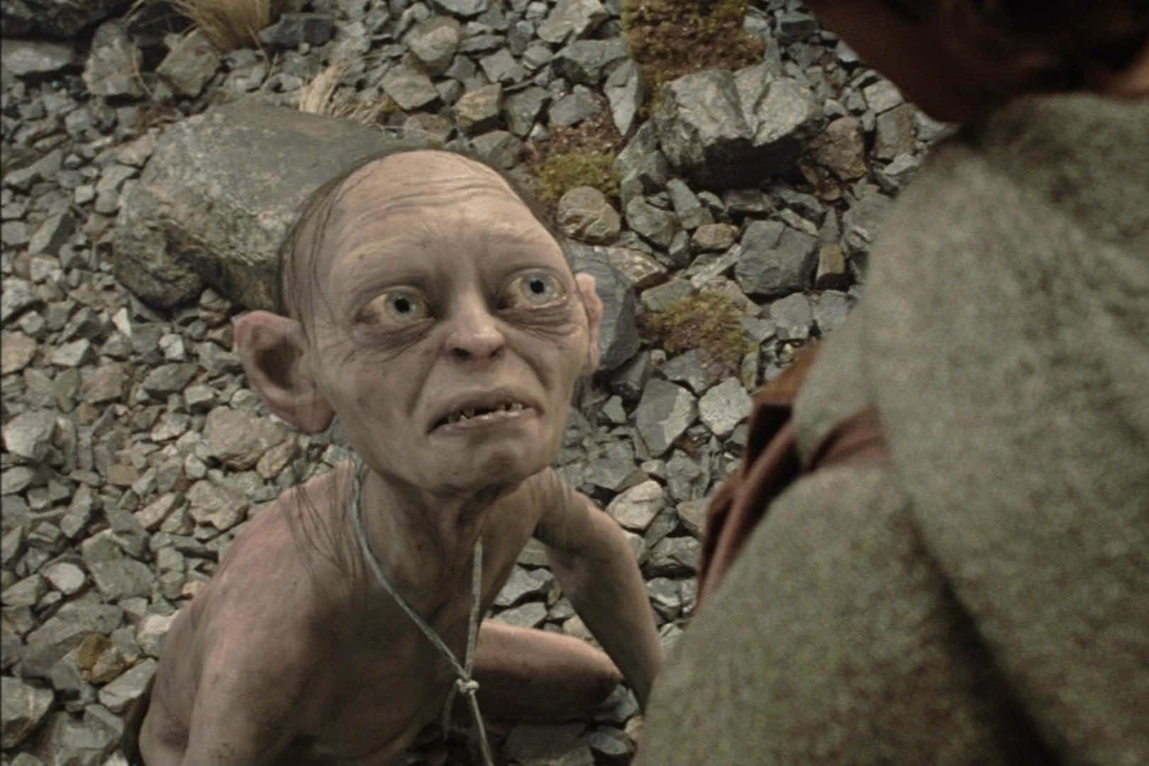 Gollum 桌布 壁紙 — 一個面色蒼白、瘦削、大眼睛、尖耳朵的哥布林蹲在岩石地上，帶著恐懼的表情向上望。