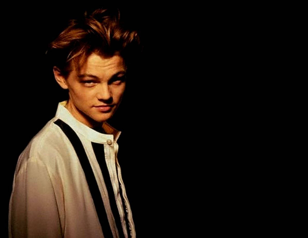 Dicaprio 桌布 壁紙 — 一個頭髮凌亂的年輕男子，身穿白襯衫和黑色吊帶，在純黑背景下凝視著。