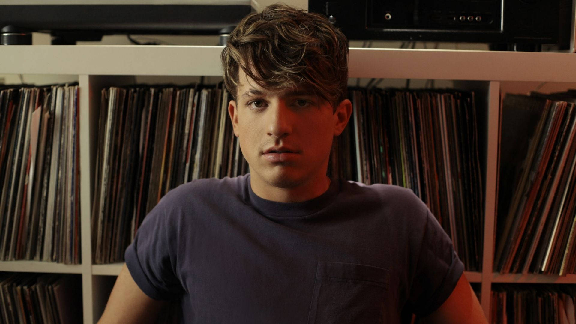Charlie Puth 桌布 壁紙 — 一個頭髮凌亂的年輕男子站在黑膠唱片牆前，專注地凝視著相機。