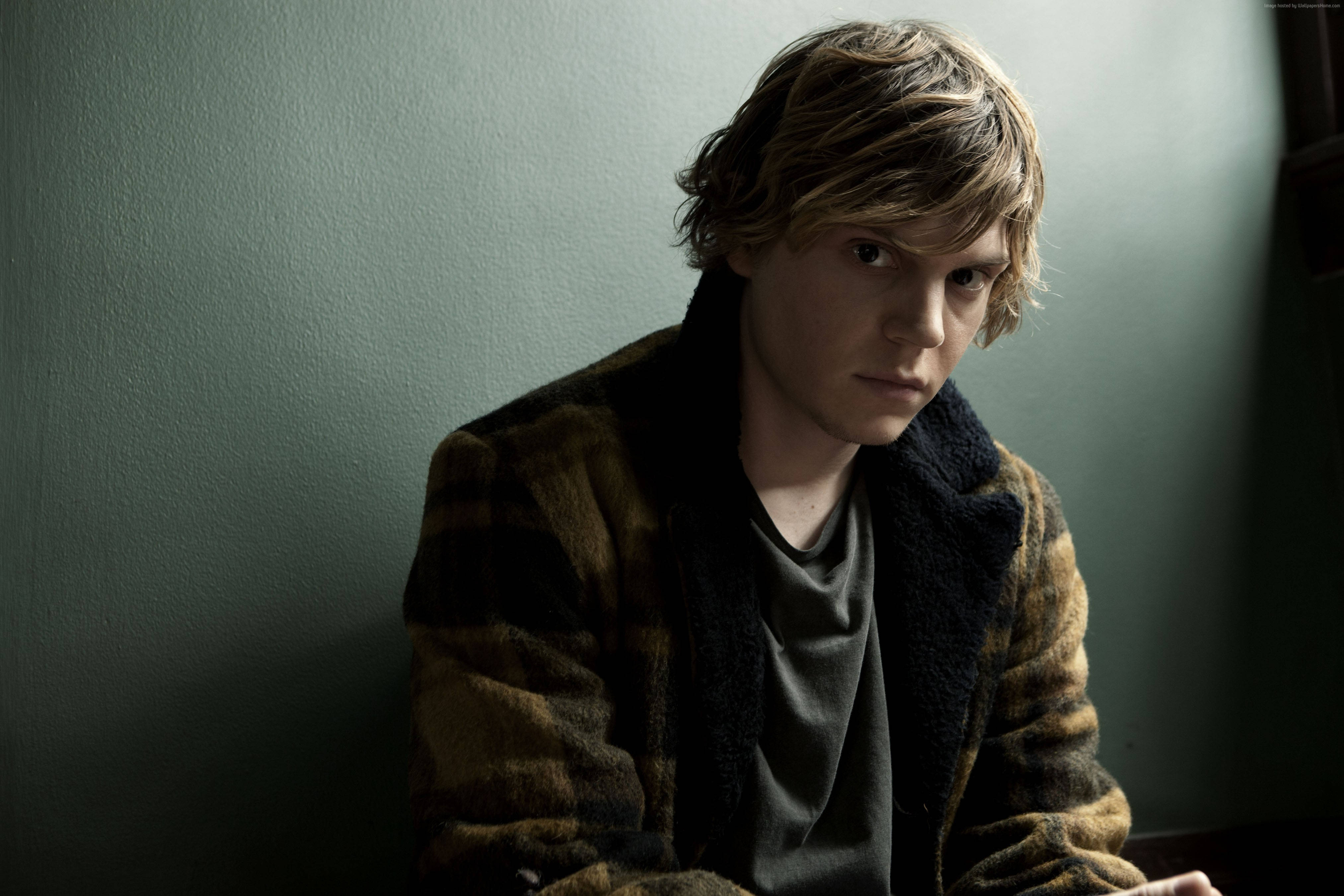 Tate Langdon 桌布 壁紙 — 一個頭髮凌亂的年輕男子靠著柔和的綠色牆壁坐著，身穿格紋外套，在柔和燈光下眼神銳利。