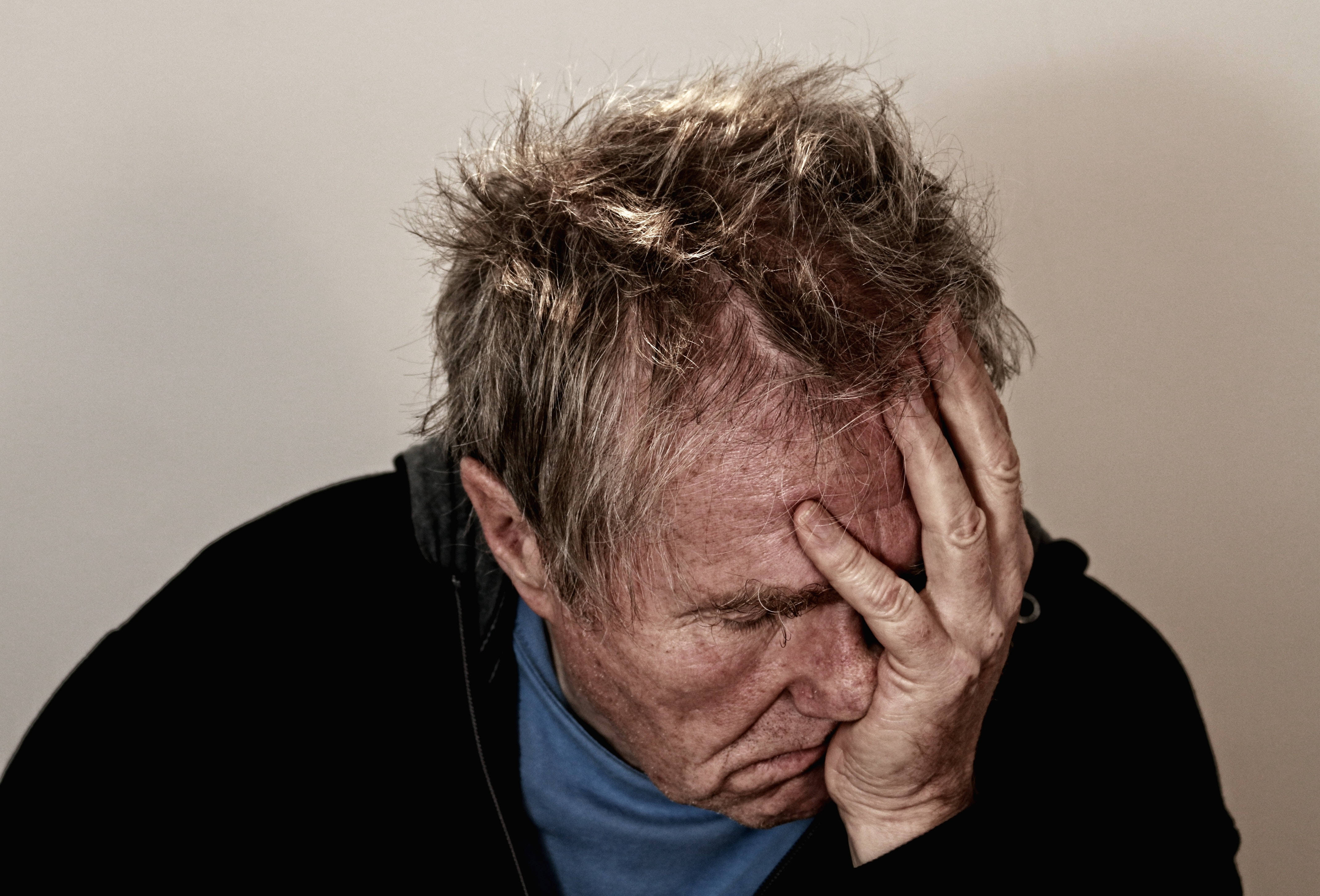 facepalm 桌布 壁紙 — 一個頭髮凌亂的男人，頭埋在手中，低頭痛苦地靠著一面素牆。