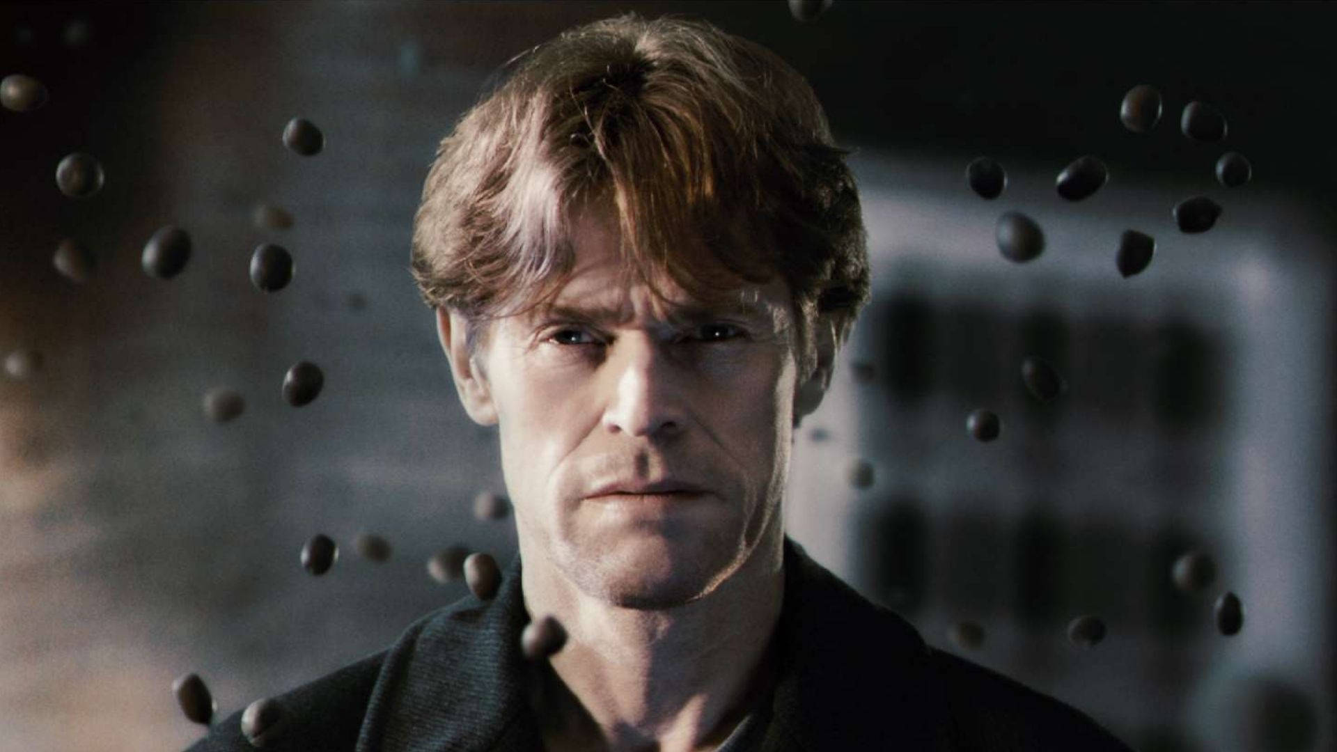 Willem Dafoe 桌布 壁紙 — 一個頭髮凌亂的男人在昏暗的城市環境中凝視著周圍漂浮的黑暗球體。