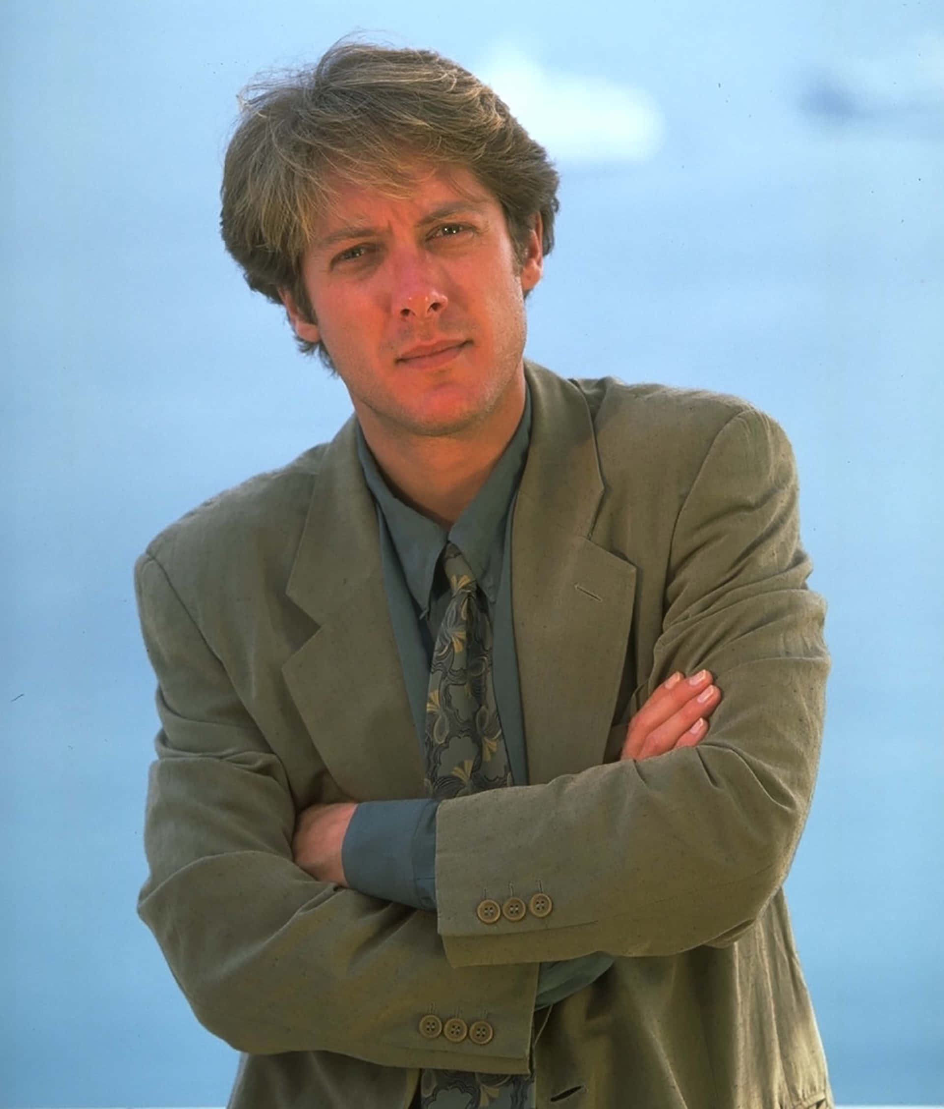 james spader 桌布 壁紙 — 一個頭髮凌亂的男人自信地交叉雙臂，背景是柔和的藍天。