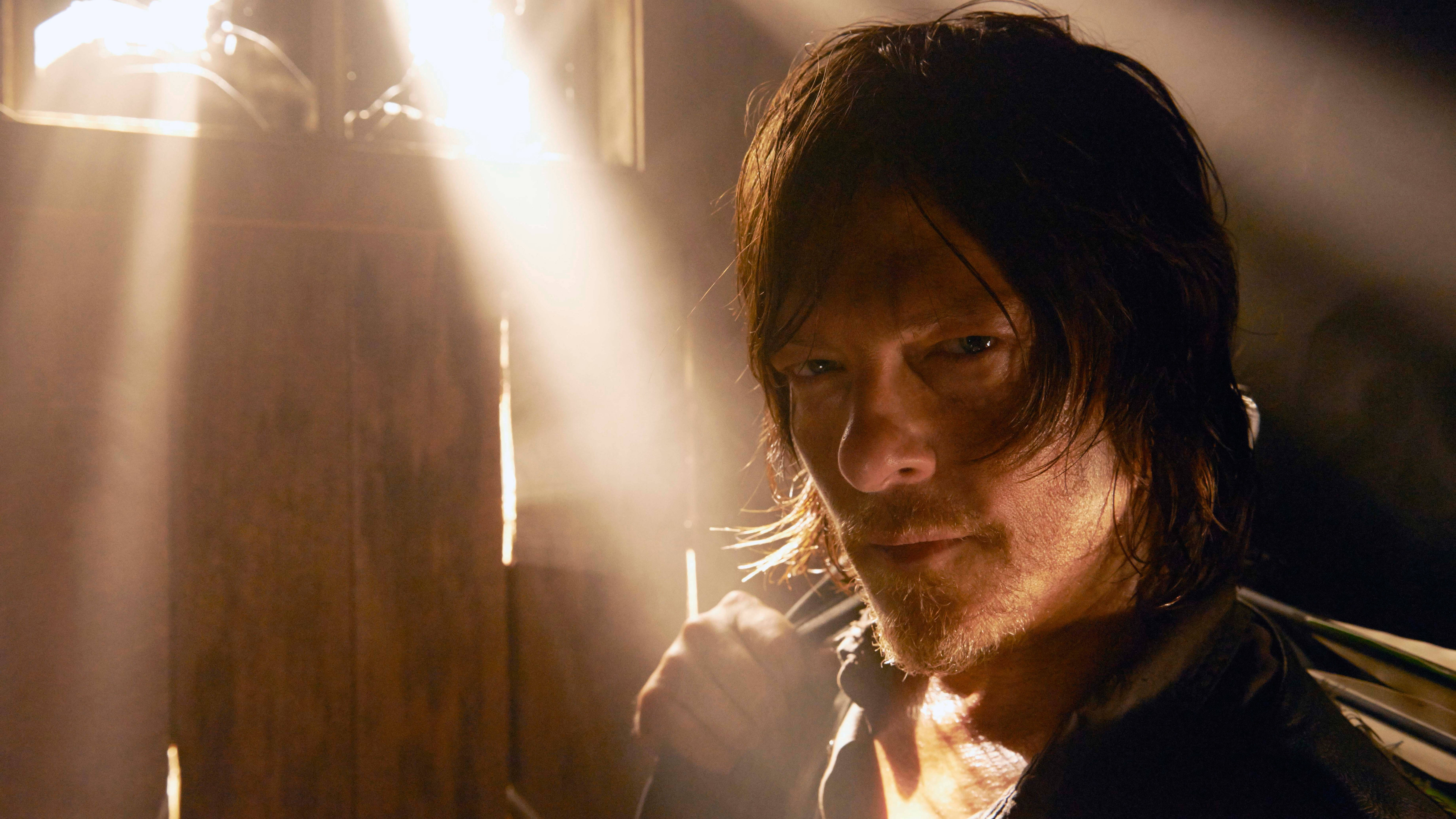 Walking Dead Daryl 桌布 壁紙 — 一個頭髮濕透、留鬍子的男人專注地凝視著，背後的窗戶透進陽光，在他臉上和木牆上投射出戲劇性的光線。