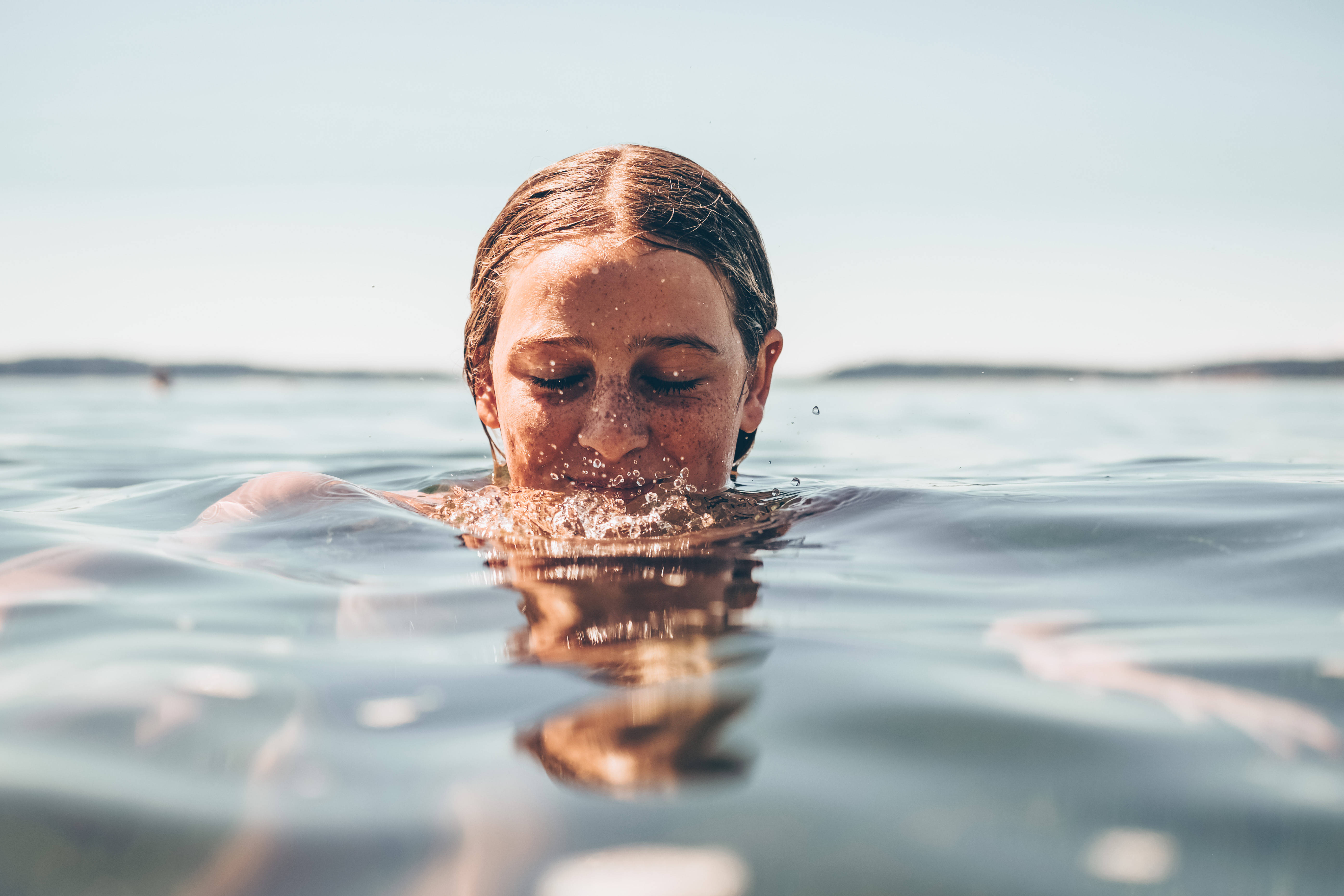 Swimming 桌布 壁紙 — 一個頭髮濕透的人在明亮日光下閉眼從平靜的藍色水中浮現。