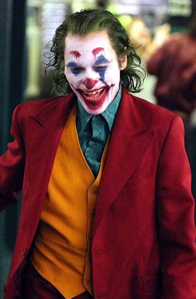 Joker Laughing 桌布 壁紙 — 一個頭髮狂野、化著小丑妝的男人，穿著紅色西裝和橙色背心，狂笑著。