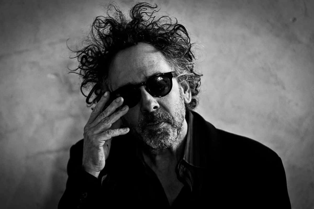 tim burton 桌布 壁紙 — 一個頭髮狂野、戴著太陽眼鏡的男人，在質感牆壁前調整眼鏡，呈現出情緒化的黑白肖像。