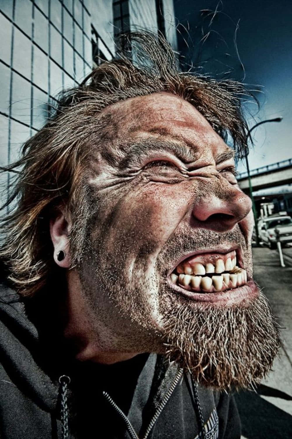 dumb 桌布 壁紙 — 一個頭髮蓬亂、鬍鬚濃密的男人在 gritty 的城市背景下激烈尖叫的特寫照片。
