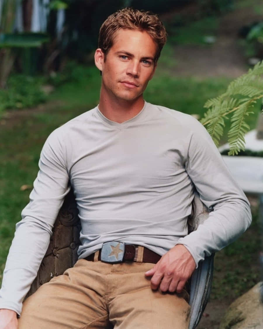 Paul Walker 桌布 壁紙 — 一個頭髮蓬亂的男人自信地坐在戶外的椅子上，穿著淺灰色長袖襯衫和卡其褲，配有一個星形扣環皮帶。