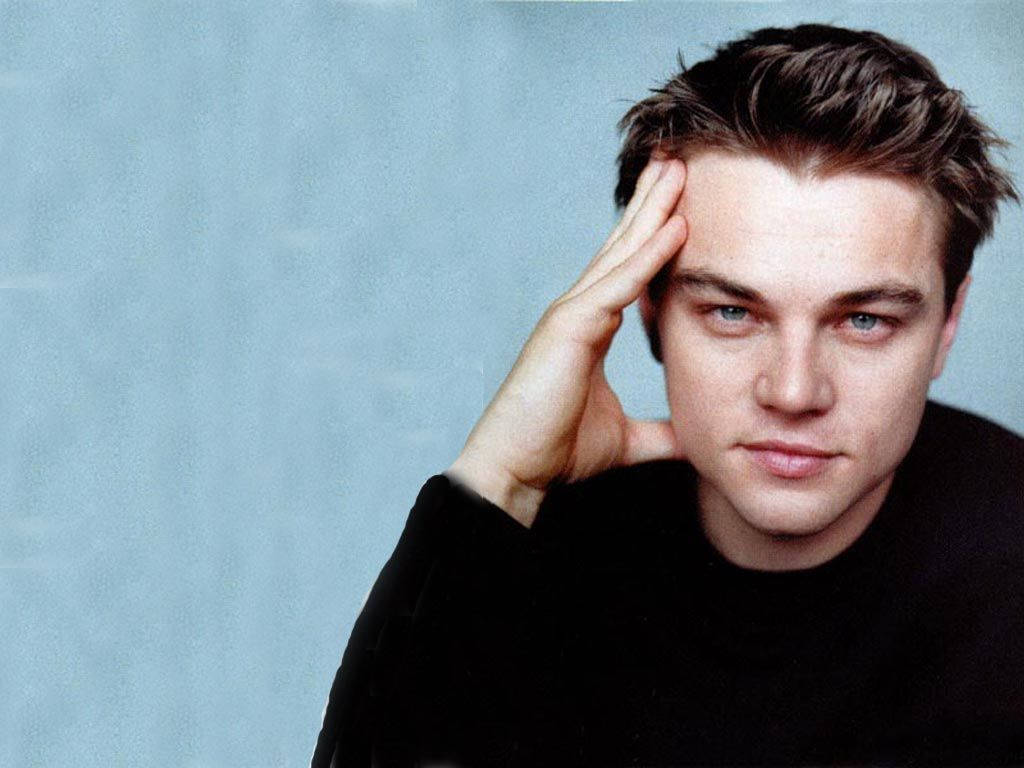 Dicaprio 桌布 壁紙 — 一個頭髮蓬鬆、藍眼睛銳利的年輕男子，在柔和的藍色攝影棚背景前將手放在額頭上。