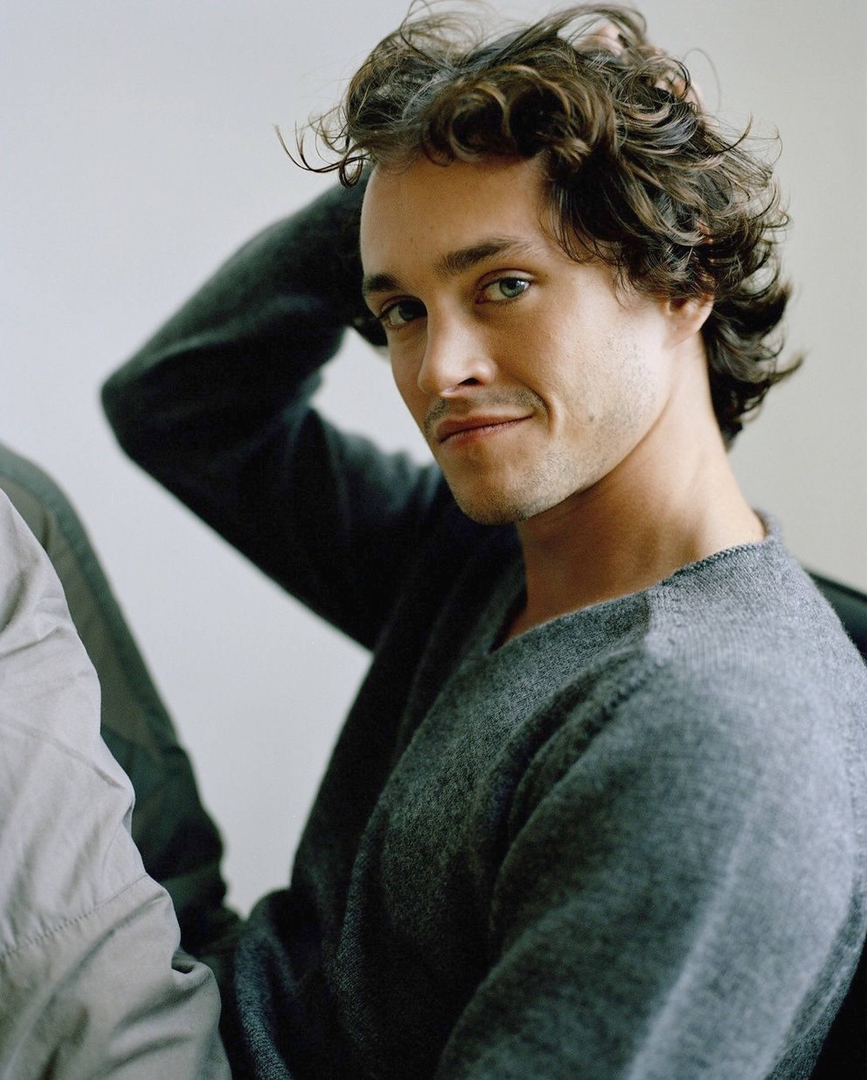 Hugh Dancy 桌布 壁紙 — 一個頭髮蓬鬆棕色、帶著溫柔微笑的男人，將手放在頭上，直視鏡頭。