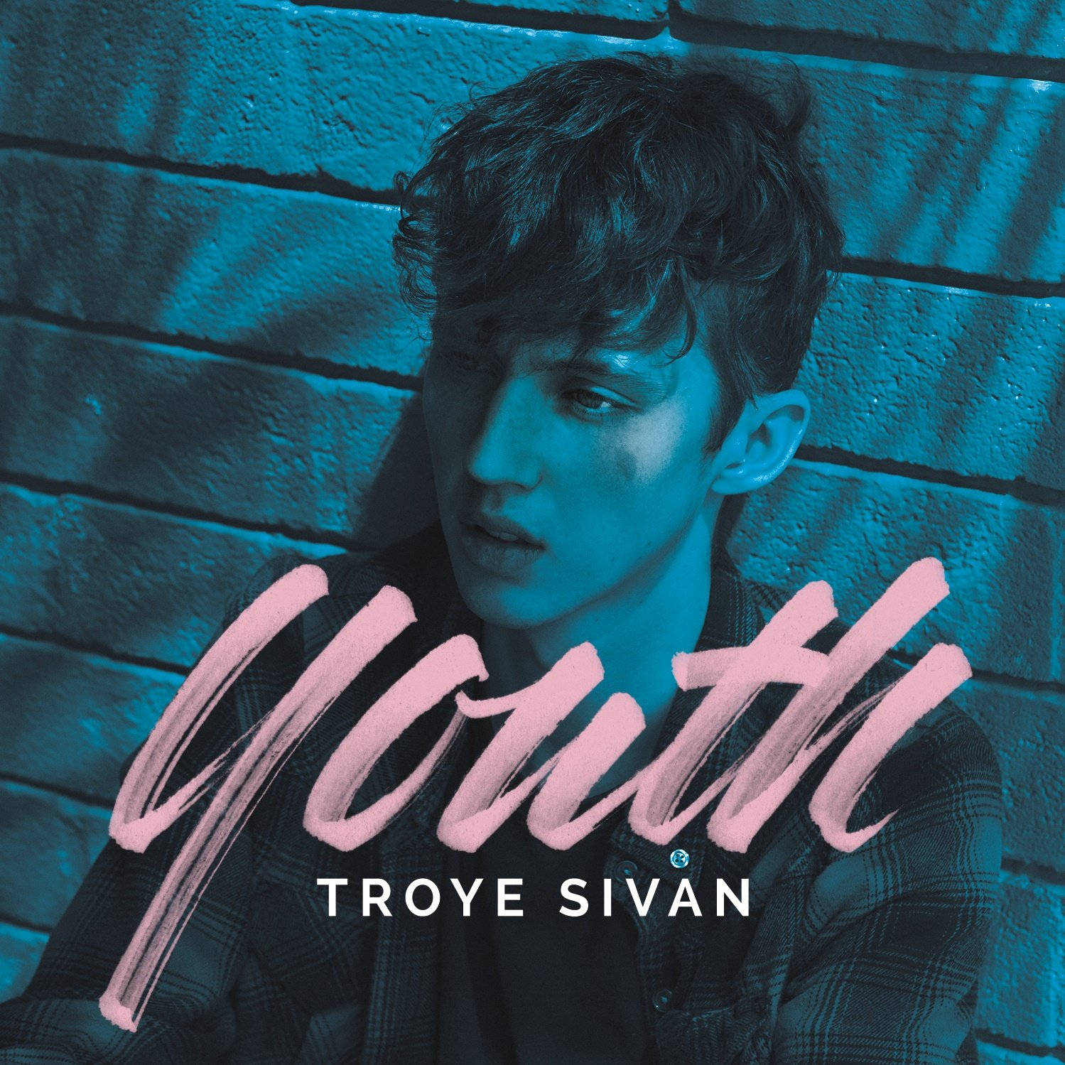 Sivan 桌布 壁紙 — 一個頭髮蓬鬆的年輕男子靠在一面有紋理的磚牆上，牆上沐浴著冷藍色的光，並帶有粉紅色文字覆蓋。