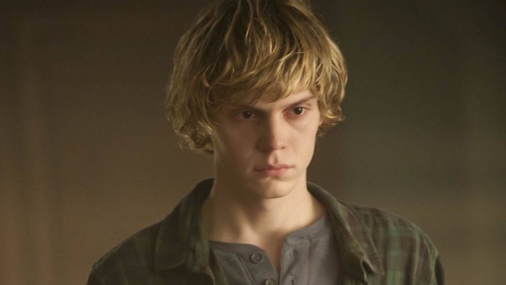 Tate Langdon 桌布 壁紙 — 一個頭髮蓬鬆的金髮年輕男子，穿著灰色亨利衫外搭格子襯衫，專注地向前凝視。